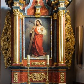 Zdjęcie nr 1: Ołtarz architektoniczny, jednondygnacyjny, jednoosiowy, ze zwieńczeniem. Ołtarz prostopadłościenny, z drewnianą mensą i kamiennym portatylem. Retabulum na niewysokim cokole o zryzalitowanych, uskokowych bokach. Retabulum ujęte parą zdwojonych filarów z przylegającymi do nich od wewnętrznej strony wąskimi pilastrami oraz parą kolumn wspierających przerwane, wyłamujące się po środku belkowanie. Zwieńczenie w formie przerwanego przyczółka w kształcie trójkąta o wklęsłych ramionach. 
Antependium,  pośrodku z motywem płaskorzeźbionego monogramu IHS i gorejącego Serca Jezusa ujętego wieńcem srebrzonych obłoków i promienistą glorią. Powierzchnia boków płyciny antependium pokryta wicią akantową. W polach cokołu dolnej kondygnacji retabulum i w dolnej partii części środkowej retabulum oraz w części belkowania ornamentyka akantowa. W górnej partii części środkowej, po środku niewielki cokolik zdobiony fragmentem wici akantowej zwieńczony półkulą z kwiatonem ujętym parą antytetycznych wolut. Dolna kondygnacja retabulum ujęta parą ażurowych, akantowych uszaków. Boki górnej kondygnacji zdobione motywem ornamentu akantowego. Partie gzymsu z ornamentyką roślinną. Pole części środkowej dolnej kondygnacji w kształcie stojącego prostokąta ujętego srebrzona i złoconą ramą w formie półwałka, zdobioną motywem liści laurowych. W środku obraz Serce Jezusa. W zwieńczeniu  rzeźbione popiersie Boga Ojca. Kondygnacja ta ujęta parą rzeźb św. Jana Chrzciciela po lewej stronie i św. Jana Ewangelisty po prawej. Po środku zwieńczenia figura Archanioła Michała. Na krawędziach przerwanego przyczółka para aniołków przyklękających na srebrzonych obłokach.
Struktura marmoryzowana w odcieniach brązów i szarości. Partie detalu architektonicznego i ornamentyka złocone i srebrzone.         
