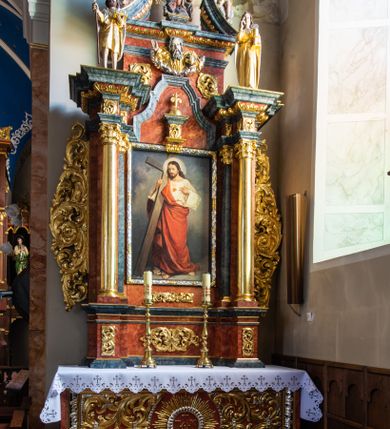 Zdjęcie nr 2: Ołtarz architektoniczny, jednondygnacyjny, jednoosiowy, ze zwieńczeniem. Ołtarz prostopadłościenny, z drewnianą mensą i kamiennym portatylem. Retabulum na niewysokim cokole o zryzalitowanych, uskokowych bokach. Retabulum ujęte parą zdwojonych filarów z przylegającymi do nich od wewnętrznej strony wąskimi pilastrami oraz parą kolumn wspierających przerwane, wyłamujące się po środku belkowanie. Zwieńczenie w formie przerwanego przyczółka w kształcie trójkąta o wklęsłych ramionach. 
Antependium,  pośrodku z motywem płaskorzeźbionego monogramu IHS i gorejącego Serca Jezusa ujętego wieńcem srebrzonych obłoków i promienistą glorią. Powierzchnia boków płyciny antependium pokryta wicią akantową. W polach cokołu dolnej kondygnacji retabulum i w dolnej partii części środkowej retabulum oraz w części belkowania ornamentyka akantowa. W górnej partii części środkowej, po środku niewielki cokolik zdobiony fragmentem wici akantowej zwieńczony półkulą z kwiatonem ujętym parą antytetycznych wolut. Dolna kondygnacja retabulum ujęta parą ażurowych, akantowych uszaków. Boki górnej kondygnacji zdobione motywem ornamentu akantowego. Partie gzymsu z ornamentyką roślinną. Pole części środkowej dolnej kondygnacji w kształcie stojącego prostokąta ujętego srebrzona i złoconą ramą w formie półwałka, zdobioną motywem liści laurowych. W środku obraz Serce Jezusa. W zwieńczeniu  rzeźbione popiersie Boga Ojca. Kondygnacja ta ujęta parą rzeźb św. Jana Chrzciciela po lewej stronie i św. Jana Ewangelisty po prawej. Po środku zwieńczenia figura Archanioła Michała. Na krawędziach przerwanego przyczółka para aniołków przyklękających na srebrzonych obłokach.
Struktura marmoryzowana w odcieniach brązów i szarości. Partie detalu architektonicznego i ornamentyka złocone i srebrzone.         
