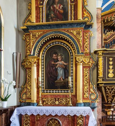 Zdjęcie nr 2: Ołtarz architektoniczny, dwukondygnacyjny, jednoosiowy, ze zwieńczeniem. Ołtarz prostopadłościenny, z drewnianą mensą i kamiennym portatylem, ujęty po bokach parą pilastrów, z antepedium dekorowanym płyciną z płaskorzeźbionym krzyżem równoramiennym z motywami lilii między ramionami, wpisanym w okrąg. Pierwsza kondygnacja nastawy w formie jednoprzelotowego łuku triumfalnego, którego półkolista arkada wsparta jest na parze kolumn o kanelowanych trzonach. Całość ujmują dwie pary spiętrzonych pilastrów oraz para spływów wolutowych, a wieńczy wydatny gzyms. Druga kondygnacja ujęta po bokach parą i kolumn wspierających wyłamujące się ponad nimi, przerwane w partii architrawu i fryzu belkowanie. Dodatkowo ta część retabulum jest flankowana parą spływów wolutowych. Zwieńczenie w formie trójkątnego przyczółka. Pola pilastrów zdobione motywem stylizowanej wici roślinnej, w kapitelach kolumn uskrzydlone główki anielskie. Podłucze arkady pierwszej kondygnacji ujęte koronkowym fryzem arkadkowym. W polu zwieńczenia płaskorzeźbiona gołębica Ducha Świętego na tle promienistej glorii. Po bokach para płomienistych wazonów, w szczycie krzyż. 
W polu pierwszej kondygnacji obraz  w kształcie stojącego prostokąta zamkniętego półkoliście, z wizerunkiem św. Józefa. W polu drugiej kondygnacji zamknięty półkoliście obraz św. Kazimierza. Struktura marmoryzowana w odcieniach brązu i niebieskości, detal architektoniczny i ornamentyka złocone i srebrzone. 
