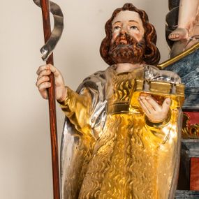 Zdjęcie nr 1: Drążona z tyłu, całopostaciowa figura św. Jana Chrzciciela stojącego frontalnie. Głowa lekko w trzech czwartych zwrócona w prawo, delikatnie odchylona do tyłu. Twarz owalna o wyrazistych rysach, z brązowym, krótkim, kręconym zarostem. Włosy brązowe, półdługie, mocno falowane, z przedziałkiem pośrodku. Święty ubrany w sięgającą kolan, złoconą skórę przewiązaną w pasie, na ramiona ma narzucony srebrzony, sięgający kolan płaszcz. W prawej dłoni trzyma brązowy krzyż na długim drzewcu, ze srebrzoną wąską szarfą. W lewej dłoni podtrzymuje zamkniętą, złoconą księgę z leżącym na niej srebrzonym barankiem. 