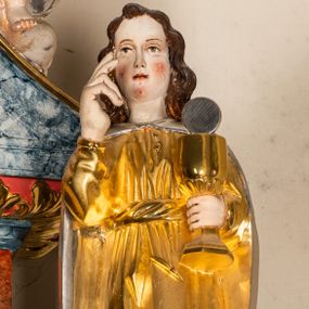 Zdjęcie nr 1: Drążona z tyłu, całopostaciowa figura św. Jana Ewangelisty stojącego frontalnie w lekkim kontrapoście. Twarz owalna o delikatnych rysach. Włosy brązowe, długie, mocno falowane. Święty jest ubrany w długą, złoconą suknię przewiązaną w pasie, na ramiona ma narzucony srebrzony, długi płaszcz spięty pod szyją. Prawa ręka w geście błogosławieństwa, w lewej dłoni złocony kielich ze srebrną hostią.  