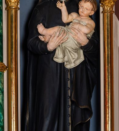 Zdjęcie nr 4: Ołtarz przyścienny, architektoniczny, jednokondygnacyjny, trójosiowy, ze zwieńczeniem. Ołtarz prostopadłościenny z antepedium artykułowanym trzema płycinami. Dwie skrajne, węższe zawierają dekorację złożoną z korony i nasadzonego na nią krzyża pomiędzy liśćmi wawrzynu ustawionymi w słup, środkowa, szersza z motywem krzyża równoramiennego o trójlistnych zakończeniach ramion, ujętego maswerkiem. Predella wklęśle zwężająca się, po bokach artykułowana pięcioma płycinami ze stylizowanymi wiciami roślinnymi. Tabernakulum w formie prostopadłościennej szafki, flankowane od frontu parą kolumienek wtopionych w naroża, zamknięte nadwieszonym łukiem półkolistym. Prostokątne, półkoliście zamknięte drzwiczki zdobione płaskorzeźbionym motywem kielicha eucharystycznego.  Część środkowa nastawy w formie trójprzelotowego łuku triumfalnego. Każda z ujmujących płytkie wnęki półkolistych arkad wsparta na parze kolumn. Podłucza ujęte dekoracyjnym ornamentem arkadkowym, który w części środkowej przybiera kształt trójliścia. Kolumny wspierają zamykające osie wimpergi. Zwieńczenie części środkowej retabulum osadzone na zdwojonym cokole, ma formę wspartej na parze kolumienek półkolistej arkady, której podłucze wypełnia motyw trójliścia, zamkniętej wimpergą. Całość ujmuje para przypór o zakończeniach ujętych kolumienkami wspierającymi sterczyny. Boczne osie zwieńczone motywem oktogonalnych latarni przekrytych kopułkami. Pola predelli zdobią motywy wici akantowych, boki ujmuje para ażurowych uszaków. W polach wimperg oraz w dolnej partii wnęki części środkowej stylizowana ornamentyka roślinna, w górnej części monogram maryjny. Krawędzie zwieńczenia zdobi motyw wici roślinnej, czołganki oraz sterczyny zwieńczone kwiatonami. We wnęce części środkowej ujęty rzeźbioną, złoconą ramą obraz Matki Boskiej z Dzieciątkiem. We wnęce po prawej stronie retabulum figura św. Stanisława Kostki, po lewej św. Alojzego Gonzagi. W zwieńczeniu figura anioła. Polichromia ołtarza utrzymana w kolorach beżu i różu, detale i ornamenty złocone. Kolumny środkowej osi zielone, marmoryzowane, gzymsy w przyczółkach w kolorach niebieskim i czerwonym.