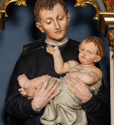 Zdjęcie nr 5: Ołtarz przyścienny, architektoniczny, jednokondygnacyjny, trójosiowy, ze zwieńczeniem. Ołtarz prostopadłościenny z antepedium artykułowanym trzema płycinami. Dwie skrajne, węższe zawierają dekorację złożoną z korony i nasadzonego na nią krzyża pomiędzy liśćmi wawrzynu ustawionymi w słup, środkowa, szersza z motywem krzyża równoramiennego o trójlistnych zakończeniach ramion, ujętego maswerkiem. Predella wklęśle zwężająca się, po bokach artykułowana pięcioma płycinami ze stylizowanymi wiciami roślinnymi. Tabernakulum w formie prostopadłościennej szafki, flankowane od frontu parą kolumienek wtopionych w naroża, zamknięte nadwieszonym łukiem półkolistym. Prostokątne, półkoliście zamknięte drzwiczki zdobione płaskorzeźbionym motywem kielicha eucharystycznego.  Część środkowa nastawy w formie trójprzelotowego łuku triumfalnego. Każda z ujmujących płytkie wnęki półkolistych arkad wsparta na parze kolumn. Podłucza ujęte dekoracyjnym ornamentem arkadkowym, który w części środkowej przybiera kształt trójliścia. Kolumny wspierają zamykające osie wimpergi. Zwieńczenie części środkowej retabulum osadzone na zdwojonym cokole, ma formę wspartej na parze kolumienek półkolistej arkady, której podłucze wypełnia motyw trójliścia, zamkniętej wimpergą. Całość ujmuje para przypór o zakończeniach ujętych kolumienkami wspierającymi sterczyny. Boczne osie zwieńczone motywem oktogonalnych latarni przekrytych kopułkami. Pola predelli zdobią motywy wici akantowych, boki ujmuje para ażurowych uszaków. W polach wimperg oraz w dolnej partii wnęki części środkowej stylizowana ornamentyka roślinna, w górnej części monogram maryjny. Krawędzie zwieńczenia zdobi motyw wici roślinnej, czołganki oraz sterczyny zwieńczone kwiatonami. We wnęce części środkowej ujęty rzeźbioną, złoconą ramą obraz Matki Boskiej z Dzieciątkiem. We wnęce po prawej stronie retabulum figura św. Stanisława Kostki, po lewej św. Alojzego Gonzagi. W zwieńczeniu figura anioła. Polichromia ołtarza utrzymana w kolorach beżu i różu, detale i ornamenty złocone. Kolumny środkowej osi zielone, marmoryzowane, gzymsy w przyczółkach w kolorach niebieskim i czerwonym.