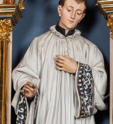 Zdjęcie nr 3: Ołtarz przyścienny, architektoniczny, jednokondygnacyjny, trójosiowy, ze zwieńczeniem. Ołtarz prostopadłościenny z antepedium artykułowanym trzema płycinami. Dwie skrajne, węższe zawierają dekorację złożoną z korony i nasadzonego na nią krzyża pomiędzy liśćmi wawrzynu ustawionymi w słup, środkowa, szersza z motywem krzyża równoramiennego o trójlistnych zakończeniach ramion, ujętego maswerkiem. Predella wklęśle zwężająca się, po bokach artykułowana pięcioma płycinami ze stylizowanymi wiciami roślinnymi. Tabernakulum w formie prostopadłościennej szafki, flankowane od frontu parą kolumienek wtopionych w naroża, zamknięte nadwieszonym łukiem półkolistym. Prostokątne, półkoliście zamknięte drzwiczki zdobione płaskorzeźbionym motywem kielicha eucharystycznego.  Część środkowa nastawy w formie trójprzelotowego łuku triumfalnego. Każda z ujmujących płytkie wnęki półkolistych arkad wsparta na parze kolumn. Podłucza ujęte dekoracyjnym ornamentem arkadkowym, który w części środkowej przybiera kształt trójliścia. Kolumny wspierają zamykające osie wimpergi. Zwieńczenie części środkowej retabulum osadzone na zdwojonym cokole, ma formę wspartej na parze kolumienek półkolistej arkady, której podłucze wypełnia motyw trójliścia, zamkniętej wimpergą. Całość ujmuje para przypór o zakończeniach ujętych kolumienkami wspierającymi sterczyny. Boczne osie zwieńczone motywem oktogonalnych latarni przekrytych kopułkami. Pola predelli zdobią motywy wici akantowych, boki ujmuje para ażurowych uszaków. W polach wimperg oraz w dolnej partii wnęki części środkowej stylizowana ornamentyka roślinna, w górnej części monogram maryjny. Krawędzie zwieńczenia zdobi motyw wici roślinnej, czołganki oraz sterczyny zwieńczone kwiatonami. We wnęce części środkowej ujęty rzeźbioną, złoconą ramą obraz Matki Boskiej z Dzieciątkiem. We wnęce po prawej stronie retabulum figura św. Stanisława Kostki, po lewej św. Alojzego Gonzagi. W zwieńczeniu figura anioła. Polichromia ołtarza utrzymana w kolorach beżu i różu, detale i ornamenty złocone. Kolumny środkowej osi zielone, marmoryzowane, gzymsy w przyczółkach w kolorach niebieskim i czerwonym.