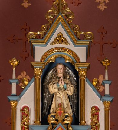 Zdjęcie nr 12: Ołtarz przyścienny, architektoniczny, jednokondygnacyjny, trójosiowy, ze zwieńczeniem. Ołtarz prostopadłościenny z antepedium artykułowanym trzema płycinami. Dwie skrajne, węższe zawierają dekorację złożoną z korony i nasadzonego na nią krzyża pomiędzy liśćmi wawrzynu ustawionymi w słup, środkowa, szersza z motywem krzyża równoramiennego o trójlistnych zakończeniach ramion, ujętego maswerkiem. Predella wklęśle zwężająca się, po bokach artykułowana pięcioma płycinami ze stylizowanymi wiciami roślinnymi. Tabernakulum w formie prostopadłościennej szafki, flankowane od frontu parą kolumienek wtopionych w naroża, zamknięte nadwieszonym łukiem półkolistym. Prostokątne, półkoliście zamknięte drzwiczki zdobione płaskorzeźbionym motywem kielicha eucharystycznego.  Część środkowa nastawy w formie trójprzelotowego łuku triumfalnego. Każda z ujmujących płytkie wnęki półkolistych arkad wsparta na parze kolumn. Podłucza ujęte dekoracyjnym ornamentem arkadkowym, który w części środkowej przybiera kształt trójliścia. Kolumny wspierają zamykające osie wimpergi. Zwieńczenie części środkowej retabulum osadzone na zdwojonym cokole, ma formę wspartej na parze kolumienek półkolistej arkady, której podłucze wypełnia motyw trójliścia, zamkniętej wimpergą. Całość ujmuje para przypór o zakończeniach ujętych kolumienkami wspierającymi sterczyny. Boczne osie zwieńczone motywem oktogonalnych latarni przekrytych kopułkami. Pola predelli zdobią motywy wici akantowych, boki ujmuje para ażurowych uszaków. W polach wimperg oraz w dolnej partii wnęki części środkowej stylizowana ornamentyka roślinna, w górnej części monogram maryjny. Krawędzie zwieńczenia zdobi motyw wici roślinnej, czołganki oraz sterczyny zwieńczone kwiatonami. We wnęce części środkowej ujęty rzeźbioną, złoconą ramą obraz Matki Boskiej z Dzieciątkiem. We wnęce po prawej stronie retabulum figura św. Stanisława Kostki, po lewej św. Alojzego Gonzagi. W zwieńczeniu figura anioła. Polichromia ołtarza utrzymana w kolorach beżu i różu, detale i ornamenty złocone. Kolumny środkowej osi zielone, marmoryzowane, gzymsy w przyczółkach w kolorach niebieskim i czerwonym.