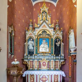 Zdjęcie nr 1: Ołtarz przyścienny, architektoniczny, jednokondygnacyjny, trójosiowy, ze zwieńczeniem. Ołtarz prostopadłościenny z antepedium artykułowanym trzema płycinami. Dwie skrajne, węższe zawierają dekorację złożoną z korony i nasadzonego na nią krzyża pomiędzy liśćmi wawrzynu ustawionymi w słup, środkowa, szersza z motywem krzyża równoramiennego o trójlistnych zakończeniach ramion, ujętego maswerkiem. Predella wklęśle zwężająca się, po bokach artykułowana pięcioma płycinami ze stylizowanymi wiciami roślinnymi. Tabernakulum w formie prostopadłościennej szafki, flankowane od frontu parą kolumienek wtopionych w naroża, zamknięte nadwieszonym łukiem półkolistym. Prostokątne, półkoliście zamknięte drzwiczki zdobione płaskorzeźbionym motywem kielicha eucharystycznego.  Część środkowa nastawy w formie trójprzelotowego łuku triumfalnego. Każda z ujmujących płytkie wnęki półkolistych arkad wsparta na parze kolumn. Podłucza ujęte dekoracyjnym ornamentem arkadkowym, który w części środkowej przybiera kształt trójliścia. Kolumny wspierają zamykające osie wimpergi. Zwieńczenie części środkowej retabulum osadzone na zdwojonym cokole, ma formę wspartej na parze kolumienek półkolistej arkady, której podłucze wypełnia motyw trójliścia, zamkniętej wimpergą. Całość ujmuje para przypór o zakończeniach ujętych kolumienkami wspierającymi sterczyny. Boczne osie zwieńczone motywem oktogonalnych latarni przekrytych kopułkami. Pola predelli zdobią motywy wici akantowych, boki ujmuje para ażurowych uszaków. W polach wimperg oraz w dolnej partii wnęki części środkowej stylizowana ornamentyka roślinna, w górnej części monogram maryjny. Krawędzie zwieńczenia zdobi motyw wici roślinnej, czołganki oraz sterczyny zwieńczone kwiatonami. We wnęce części środkowej ujęty rzeźbioną, złoconą ramą obraz Matki Boskiej z Dzieciątkiem. We wnęce po prawej stronie retabulum figura św. Stanisława Kostki, po lewej św. Alojzego Gonzagi. W zwieńczeniu figura anioła. Polichromia ołtarza utrzymana w kolorach beżu i różu, detale i ornamenty złocone. Kolumny środkowej osi zielone, marmoryzowane, gzymsy w przyczółkach w kolorach niebieskim i czerwonym.