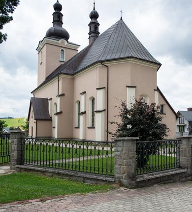 Zdjęcie nr 24: Kościół orientowany, jest budowlą murowaną z cegły i kamienia, na rzucie podłużnym. Korpus nawowy jest jednonawowy i czteroprzęsłowy. Do dwuprzęsłowego, zamkniętego trójbocznie prezbiterium od północy przylega zakrystia. Na osi kościoła, w przedłużeniu północnego przęsła jest czworoboczna, wysunięta przed lico fasady wieża. Od południa do drugiego przęsła korpusu przylega kruchta. Nawa przekryta jest sklepieniem kolebkowym z lunetami wspartymi na pilastrach, w prezbiterium sklepienie krzyżowo-żebrowe z gurtą wspartą na pilastrach. Przestrzeń prezbiterium od korpusu nawowego oddziela półkolista arkada łuku tęczowego i drewniana balustrada. Artykulację ścian na zewnątrz kościoła stanowi zespół dwuuskokowych przypór, w narożach wieży są czterouskokowe, osadzonych na niewysokim cokole. Do wnętrza prowadzą 3 otwory drzwiowe. Dwuskrzydłowe drzwi w fasadzie ujęte są kamiennym obramieniem zamkniętym łukiem koszowym z kluczem pośrodku, wspartym na gzymsie oraz 2 w północnej ścianie kaplicy bocznej. 2 prostokątne prowadzą przez kruchtę i zakrystię. Ściany korpusu nawowego i prezbiterium przeprute są prostokątnymi oknami zamkniętymi łukiem odcinkowym. Okno na zakończeniu prezbiterium jest formie półkoliście zamkniętej niszy z figurą Matki Boskiej. Kształt okien korpusu i prezbiterium został powtórzony w przyległości prezbiterium. Powyżej wejścia na osi wieży małe okienko zamknięte łukiem koszowym, wyżej nisza zamknięta ostrołukowo. W górnej partii wieży znajdują się cztery, duże, zamknięte półkoliście otwory okienne ujęte prostymi obramieniami. Szczyt wierzy obiega gzyms wieńczący z półkolistym łukiem na osi każdej ze ścian. Dach w formie hełmu z latarnią. Dach prezbiterium i korpusu dwuspadowy, kryty blachą, nad pierwszym przęsłem wieżyczka na sygnaturkę. Kruchta z dachem dwuspadowym, przyległość pulpitowym. Tynki w kolorze beżowym i białym. 