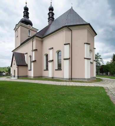 Zdjęcie nr 35: Kościół orientowany, jest budowlą murowaną z cegły i kamienia, na rzucie podłużnym. Korpus nawowy jest jednonawowy i czteroprzęsłowy. Do dwuprzęsłowego, zamkniętego trójbocznie prezbiterium od północy przylega zakrystia. Na osi kościoła, w przedłużeniu północnego przęsła jest czworoboczna, wysunięta przed lico fasady wieża. Od południa do drugiego przęsła korpusu przylega kruchta. Nawa przekryta jest sklepieniem kolebkowym z lunetami wspartymi na pilastrach, w prezbiterium sklepienie krzyżowo-żebrowe z gurtą wspartą na pilastrach. Przestrzeń prezbiterium od korpusu nawowego oddziela półkolista arkada łuku tęczowego i drewniana balustrada. Artykulację ścian na zewnątrz kościoła stanowi zespół dwuuskokowych przypór, w narożach wieży są czterouskokowe, osadzonych na niewysokim cokole. Do wnętrza prowadzą 3 otwory drzwiowe. Dwuskrzydłowe drzwi w fasadzie ujęte są kamiennym obramieniem zamkniętym łukiem koszowym z kluczem pośrodku, wspartym na gzymsie oraz 2 w północnej ścianie kaplicy bocznej. 2 prostokątne prowadzą przez kruchtę i zakrystię. Ściany korpusu nawowego i prezbiterium przeprute są prostokątnymi oknami zamkniętymi łukiem odcinkowym. Okno na zakończeniu prezbiterium jest formie półkoliście zamkniętej niszy z figurą Matki Boskiej. Kształt okien korpusu i prezbiterium został powtórzony w przyległości prezbiterium. Powyżej wejścia na osi wieży małe okienko zamknięte łukiem koszowym, wyżej nisza zamknięta ostrołukowo. W górnej partii wieży znajdują się cztery, duże, zamknięte półkoliście otwory okienne ujęte prostymi obramieniami. Szczyt wierzy obiega gzyms wieńczący z półkolistym łukiem na osi każdej ze ścian. Dach w formie hełmu z latarnią. Dach prezbiterium i korpusu dwuspadowy, kryty blachą, nad pierwszym przęsłem wieżyczka na sygnaturkę. Kruchta z dachem dwuspadowym, przyległość pulpitowym. Tynki w kolorze beżowym i białym. 