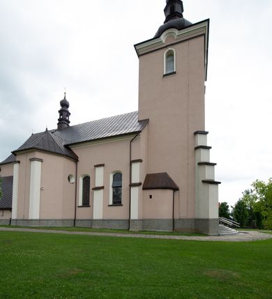 Zdjęcie nr 11: Kościół orientowany, jest budowlą murowaną z cegły i kamienia, na rzucie podłużnym. Korpus nawowy jest jednonawowy i czteroprzęsłowy. Do dwuprzęsłowego, zamkniętego trójbocznie prezbiterium od północy przylega zakrystia. Na osi kościoła, w przedłużeniu północnego przęsła jest czworoboczna, wysunięta przed lico fasady wieża. Od południa do drugiego przęsła korpusu przylega kruchta. Nawa przekryta jest sklepieniem kolebkowym z lunetami wspartymi na pilastrach, w prezbiterium sklepienie krzyżowo-żebrowe z gurtą wspartą na pilastrach. Przestrzeń prezbiterium od korpusu nawowego oddziela półkolista arkada łuku tęczowego i drewniana balustrada. Artykulację ścian na zewnątrz kościoła stanowi zespół dwuuskokowych przypór, w narożach wieży są czterouskokowe, osadzonych na niewysokim cokole. Do wnętrza prowadzą 3 otwory drzwiowe. Dwuskrzydłowe drzwi w fasadzie ujęte są kamiennym obramieniem zamkniętym łukiem koszowym z kluczem pośrodku, wspartym na gzymsie oraz 2 w północnej ścianie kaplicy bocznej. 2 prostokątne prowadzą przez kruchtę i zakrystię. Ściany korpusu nawowego i prezbiterium przeprute są prostokątnymi oknami zamkniętymi łukiem odcinkowym. Okno na zakończeniu prezbiterium jest formie półkoliście zamkniętej niszy z figurą Matki Boskiej. Kształt okien korpusu i prezbiterium został powtórzony w przyległości prezbiterium. Powyżej wejścia na osi wieży małe okienko zamknięte łukiem koszowym, wyżej nisza zamknięta ostrołukowo. W górnej partii wieży znajdują się cztery, duże, zamknięte półkoliście otwory okienne ujęte prostymi obramieniami. Szczyt wierzy obiega gzyms wieńczący z półkolistym łukiem na osi każdej ze ścian. Dach w formie hełmu z latarnią. Dach prezbiterium i korpusu dwuspadowy, kryty blachą, nad pierwszym przęsłem wieżyczka na sygnaturkę. Kruchta z dachem dwuspadowym, przyległość pulpitowym. Tynki w kolorze beżowym i białym. 