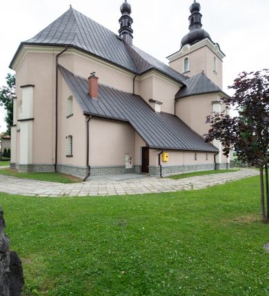 Zdjęcie nr 51: Kościół orientowany, jest budowlą murowaną z cegły i kamienia, na rzucie podłużnym. Korpus nawowy jest jednonawowy i czteroprzęsłowy. Do dwuprzęsłowego, zamkniętego trójbocznie prezbiterium od północy przylega zakrystia. Na osi kościoła, w przedłużeniu północnego przęsła jest czworoboczna, wysunięta przed lico fasady wieża. Od południa do drugiego przęsła korpusu przylega kruchta. Nawa przekryta jest sklepieniem kolebkowym z lunetami wspartymi na pilastrach, w prezbiterium sklepienie krzyżowo-żebrowe z gurtą wspartą na pilastrach. Przestrzeń prezbiterium od korpusu nawowego oddziela półkolista arkada łuku tęczowego i drewniana balustrada. Artykulację ścian na zewnątrz kościoła stanowi zespół dwuuskokowych przypór, w narożach wieży są czterouskokowe, osadzonych na niewysokim cokole. Do wnętrza prowadzą 3 otwory drzwiowe. Dwuskrzydłowe drzwi w fasadzie ujęte są kamiennym obramieniem zamkniętym łukiem koszowym z kluczem pośrodku, wspartym na gzymsie oraz 2 w północnej ścianie kaplicy bocznej. 2 prostokątne prowadzą przez kruchtę i zakrystię. Ściany korpusu nawowego i prezbiterium przeprute są prostokątnymi oknami zamkniętymi łukiem odcinkowym. Okno na zakończeniu prezbiterium jest formie półkoliście zamkniętej niszy z figurą Matki Boskiej. Kształt okien korpusu i prezbiterium został powtórzony w przyległości prezbiterium. Powyżej wejścia na osi wieży małe okienko zamknięte łukiem koszowym, wyżej nisza zamknięta ostrołukowo. W górnej partii wieży znajdują się cztery, duże, zamknięte półkoliście otwory okienne ujęte prostymi obramieniami. Szczyt wierzy obiega gzyms wieńczący z półkolistym łukiem na osi każdej ze ścian. Dach w formie hełmu z latarnią. Dach prezbiterium i korpusu dwuspadowy, kryty blachą, nad pierwszym przęsłem wieżyczka na sygnaturkę. Kruchta z dachem dwuspadowym, przyległość pulpitowym. Tynki w kolorze beżowym i białym. 