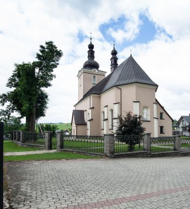 Zdjęcie nr 2: Kościół orientowany, jest budowlą murowaną z cegły i kamienia, na rzucie podłużnym. Korpus nawowy jest jednonawowy i czteroprzęsłowy. Do dwuprzęsłowego, zamkniętego trójbocznie prezbiterium od północy przylega zakrystia. Na osi kościoła, w przedłużeniu północnego przęsła jest czworoboczna, wysunięta przed lico fasady wieża. Od południa do drugiego przęsła korpusu przylega kruchta. Nawa przekryta jest sklepieniem kolebkowym z lunetami wspartymi na pilastrach, w prezbiterium sklepienie krzyżowo-żebrowe z gurtą wspartą na pilastrach. Przestrzeń prezbiterium od korpusu nawowego oddziela półkolista arkada łuku tęczowego i drewniana balustrada. Artykulację ścian na zewnątrz kościoła stanowi zespół dwuuskokowych przypór, w narożach wieży są czterouskokowe, osadzonych na niewysokim cokole. Do wnętrza prowadzą 3 otwory drzwiowe. Dwuskrzydłowe drzwi w fasadzie ujęte są kamiennym obramieniem zamkniętym łukiem koszowym z kluczem pośrodku, wspartym na gzymsie oraz 2 w północnej ścianie kaplicy bocznej. 2 prostokątne prowadzą przez kruchtę i zakrystię. Ściany korpusu nawowego i prezbiterium przeprute są prostokątnymi oknami zamkniętymi łukiem odcinkowym. Okno na zakończeniu prezbiterium jest formie półkoliście zamkniętej niszy z figurą Matki Boskiej. Kształt okien korpusu i prezbiterium został powtórzony w przyległości prezbiterium. Powyżej wejścia na osi wieży małe okienko zamknięte łukiem koszowym, wyżej nisza zamknięta ostrołukowo. W górnej partii wieży znajdują się cztery, duże, zamknięte półkoliście otwory okienne ujęte prostymi obramieniami. Szczyt wierzy obiega gzyms wieńczący z półkolistym łukiem na osi każdej ze ścian. Dach w formie hełmu z latarnią. Dach prezbiterium i korpusu dwuspadowy, kryty blachą, nad pierwszym przęsłem wieżyczka na sygnaturkę. Kruchta z dachem dwuspadowym, przyległość pulpitowym. Tynki w kolorze beżowym i białym. 