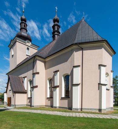 Zdjęcie nr 1: Kościół orientowany, jest budowlą murowaną z cegły i kamienia, na rzucie podłużnym. Korpus nawowy jest jednonawowy i czteroprzęsłowy. Do dwuprzęsłowego, zamkniętego trójbocznie prezbiterium od północy przylega zakrystia. Na osi kościoła, w przedłużeniu północnego przęsła jest czworoboczna, wysunięta przed lico fasady wieża. Od południa do drugiego przęsła korpusu przylega kruchta. Nawa przekryta jest sklepieniem kolebkowym z lunetami wspartymi na pilastrach, w prezbiterium sklepienie krzyżowo-żebrowe z gurtą wspartą na pilastrach. Przestrzeń prezbiterium od korpusu nawowego oddziela półkolista arkada łuku tęczowego i drewniana balustrada. Artykulację ścian na zewnątrz kościoła stanowi zespół dwuuskokowych przypór, w narożach wieży są czterouskokowe, osadzonych na niewysokim cokole. Do wnętrza prowadzą 3 otwory drzwiowe. Dwuskrzydłowe drzwi w fasadzie ujęte są kamiennym obramieniem zamkniętym łukiem koszowym z kluczem pośrodku, wspartym na gzymsie oraz 2 w północnej ścianie kaplicy bocznej. 2 prostokątne prowadzą przez kruchtę i zakrystię. Ściany korpusu nawowego i prezbiterium przeprute są prostokątnymi oknami zamkniętymi łukiem odcinkowym. Okno na zakończeniu prezbiterium jest formie półkoliście zamkniętej niszy z figurą Matki Boskiej. Kształt okien korpusu i prezbiterium został powtórzony w przyległości prezbiterium. Powyżej wejścia na osi wieży małe okienko zamknięte łukiem koszowym, wyżej nisza zamknięta ostrołukowo. W górnej partii wieży znajdują się cztery, duże, zamknięte półkoliście otwory okienne ujęte prostymi obramieniami. Szczyt wierzy obiega gzyms wieńczący z półkolistym łukiem na osi każdej ze ścian. Dach w formie hełmu z latarnią. Dach prezbiterium i korpusu dwuspadowy, kryty blachą, nad pierwszym przęsłem wieżyczka na sygnaturkę. Kruchta z dachem dwuspadowym, przyległość pulpitowym. Tynki w kolorze beżowym i białym. 