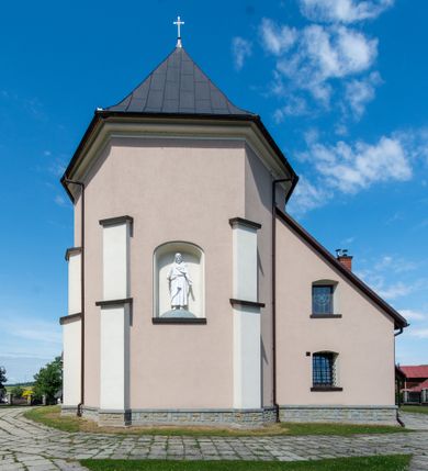 Zdjęcie nr 17: Kościół orientowany, jest budowlą murowaną z cegły i kamienia, na rzucie podłużnym. Korpus nawowy jest jednonawowy i czteroprzęsłowy. Do dwuprzęsłowego, zamkniętego trójbocznie prezbiterium od północy przylega zakrystia. Na osi kościoła, w przedłużeniu północnego przęsła jest czworoboczna, wysunięta przed lico fasady wieża. Od południa do drugiego przęsła korpusu przylega kruchta. Nawa przekryta jest sklepieniem kolebkowym z lunetami wspartymi na pilastrach, w prezbiterium sklepienie krzyżowo-żebrowe z gurtą wspartą na pilastrach. Przestrzeń prezbiterium od korpusu nawowego oddziela półkolista arkada łuku tęczowego i drewniana balustrada. Artykulację ścian na zewnątrz kościoła stanowi zespół dwuuskokowych przypór, w narożach wieży są czterouskokowe, osadzonych na niewysokim cokole. Do wnętrza prowadzą 3 otwory drzwiowe. Dwuskrzydłowe drzwi w fasadzie ujęte są kamiennym obramieniem zamkniętym łukiem koszowym z kluczem pośrodku, wspartym na gzymsie oraz 2 w północnej ścianie kaplicy bocznej. 2 prostokątne prowadzą przez kruchtę i zakrystię. Ściany korpusu nawowego i prezbiterium przeprute są prostokątnymi oknami zamkniętymi łukiem odcinkowym. Okno na zakończeniu prezbiterium jest formie półkoliście zamkniętej niszy z figurą Matki Boskiej. Kształt okien korpusu i prezbiterium został powtórzony w przyległości prezbiterium. Powyżej wejścia na osi wieży małe okienko zamknięte łukiem koszowym, wyżej nisza zamknięta ostrołukowo. W górnej partii wieży znajdują się cztery, duże, zamknięte półkoliście otwory okienne ujęte prostymi obramieniami. Szczyt wierzy obiega gzyms wieńczący z półkolistym łukiem na osi każdej ze ścian. Dach w formie hełmu z latarnią. Dach prezbiterium i korpusu dwuspadowy, kryty blachą, nad pierwszym przęsłem wieżyczka na sygnaturkę. Kruchta z dachem dwuspadowym, przyległość pulpitowym. Tynki w kolorze beżowym i białym. 