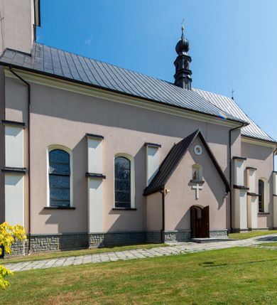 Zdjęcie nr 18: Kościół orientowany, jest budowlą murowaną z cegły i kamienia, na rzucie podłużnym. Korpus nawowy jest jednonawowy i czteroprzęsłowy. Do dwuprzęsłowego, zamkniętego trójbocznie prezbiterium od północy przylega zakrystia. Na osi kościoła, w przedłużeniu północnego przęsła jest czworoboczna, wysunięta przed lico fasady wieża. Od południa do drugiego przęsła korpusu przylega kruchta. Nawa przekryta jest sklepieniem kolebkowym z lunetami wspartymi na pilastrach, w prezbiterium sklepienie krzyżowo-żebrowe z gurtą wspartą na pilastrach. Przestrzeń prezbiterium od korpusu nawowego oddziela półkolista arkada łuku tęczowego i drewniana balustrada. Artykulację ścian na zewnątrz kościoła stanowi zespół dwuuskokowych przypór, w narożach wieży są czterouskokowe, osadzonych na niewysokim cokole. Do wnętrza prowadzą 3 otwory drzwiowe. Dwuskrzydłowe drzwi w fasadzie ujęte są kamiennym obramieniem zamkniętym łukiem koszowym z kluczem pośrodku, wspartym na gzymsie oraz 2 w północnej ścianie kaplicy bocznej. 2 prostokątne prowadzą przez kruchtę i zakrystię. Ściany korpusu nawowego i prezbiterium przeprute są prostokątnymi oknami zamkniętymi łukiem odcinkowym. Okno na zakończeniu prezbiterium jest formie półkoliście zamkniętej niszy z figurą Matki Boskiej. Kształt okien korpusu i prezbiterium został powtórzony w przyległości prezbiterium. Powyżej wejścia na osi wieży małe okienko zamknięte łukiem koszowym, wyżej nisza zamknięta ostrołukowo. W górnej partii wieży znajdują się cztery, duże, zamknięte półkoliście otwory okienne ujęte prostymi obramieniami. Szczyt wierzy obiega gzyms wieńczący z półkolistym łukiem na osi każdej ze ścian. Dach w formie hełmu z latarnią. Dach prezbiterium i korpusu dwuspadowy, kryty blachą, nad pierwszym przęsłem wieżyczka na sygnaturkę. Kruchta z dachem dwuspadowym, przyległość pulpitowym. Tynki w kolorze beżowym i białym. 