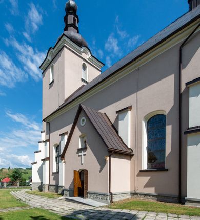 Zdjęcie nr 20: Kościół orientowany, jest budowlą murowaną z cegły i kamienia, na rzucie podłużnym. Korpus nawowy jest jednonawowy i czteroprzęsłowy. Do dwuprzęsłowego, zamkniętego trójbocznie prezbiterium od północy przylega zakrystia. Na osi kościoła, w przedłużeniu północnego przęsła jest czworoboczna, wysunięta przed lico fasady wieża. Od południa do drugiego przęsła korpusu przylega kruchta. Nawa przekryta jest sklepieniem kolebkowym z lunetami wspartymi na pilastrach, w prezbiterium sklepienie krzyżowo-żebrowe z gurtą wspartą na pilastrach. Przestrzeń prezbiterium od korpusu nawowego oddziela półkolista arkada łuku tęczowego i drewniana balustrada. Artykulację ścian na zewnątrz kościoła stanowi zespół dwuuskokowych przypór, w narożach wieży są czterouskokowe, osadzonych na niewysokim cokole. Do wnętrza prowadzą 3 otwory drzwiowe. Dwuskrzydłowe drzwi w fasadzie ujęte są kamiennym obramieniem zamkniętym łukiem koszowym z kluczem pośrodku, wspartym na gzymsie oraz 2 w północnej ścianie kaplicy bocznej. 2 prostokątne prowadzą przez kruchtę i zakrystię. Ściany korpusu nawowego i prezbiterium przeprute są prostokątnymi oknami zamkniętymi łukiem odcinkowym. Okno na zakończeniu prezbiterium jest formie półkoliście zamkniętej niszy z figurą Matki Boskiej. Kształt okien korpusu i prezbiterium został powtórzony w przyległości prezbiterium. Powyżej wejścia na osi wieży małe okienko zamknięte łukiem koszowym, wyżej nisza zamknięta ostrołukowo. W górnej partii wieży znajdują się cztery, duże, zamknięte półkoliście otwory okienne ujęte prostymi obramieniami. Szczyt wierzy obiega gzyms wieńczący z półkolistym łukiem na osi każdej ze ścian. Dach w formie hełmu z latarnią. Dach prezbiterium i korpusu dwuspadowy, kryty blachą, nad pierwszym przęsłem wieżyczka na sygnaturkę. Kruchta z dachem dwuspadowym, przyległość pulpitowym. Tynki w kolorze beżowym i białym. 