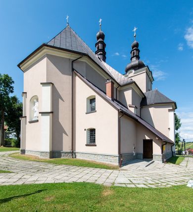 Zdjęcie nr 52: Kościół orientowany, jest budowlą murowaną z cegły i kamienia, na rzucie podłużnym. Korpus nawowy jest jednonawowy i czteroprzęsłowy. Do dwuprzęsłowego, zamkniętego trójbocznie prezbiterium od północy przylega zakrystia. Na osi kościoła, w przedłużeniu północnego przęsła jest czworoboczna, wysunięta przed lico fasady wieża. Od południa do drugiego przęsła korpusu przylega kruchta. Nawa przekryta jest sklepieniem kolebkowym z lunetami wspartymi na pilastrach, w prezbiterium sklepienie krzyżowo-żebrowe z gurtą wspartą na pilastrach. Przestrzeń prezbiterium od korpusu nawowego oddziela półkolista arkada łuku tęczowego i drewniana balustrada. Artykulację ścian na zewnątrz kościoła stanowi zespół dwuuskokowych przypór, w narożach wieży są czterouskokowe, osadzonych na niewysokim cokole. Do wnętrza prowadzą 3 otwory drzwiowe. Dwuskrzydłowe drzwi w fasadzie ujęte są kamiennym obramieniem zamkniętym łukiem koszowym z kluczem pośrodku, wspartym na gzymsie oraz 2 w północnej ścianie kaplicy bocznej. 2 prostokątne prowadzą przez kruchtę i zakrystię. Ściany korpusu nawowego i prezbiterium przeprute są prostokątnymi oknami zamkniętymi łukiem odcinkowym. Okno na zakończeniu prezbiterium jest formie półkoliście zamkniętej niszy z figurą Matki Boskiej. Kształt okien korpusu i prezbiterium został powtórzony w przyległości prezbiterium. Powyżej wejścia na osi wieży małe okienko zamknięte łukiem koszowym, wyżej nisza zamknięta ostrołukowo. W górnej partii wieży znajdują się cztery, duże, zamknięte półkoliście otwory okienne ujęte prostymi obramieniami. Szczyt wierzy obiega gzyms wieńczący z półkolistym łukiem na osi każdej ze ścian. Dach w formie hełmu z latarnią. Dach prezbiterium i korpusu dwuspadowy, kryty blachą, nad pierwszym przęsłem wieżyczka na sygnaturkę. Kruchta z dachem dwuspadowym, przyległość pulpitowym. Tynki w kolorze beżowym i białym. 