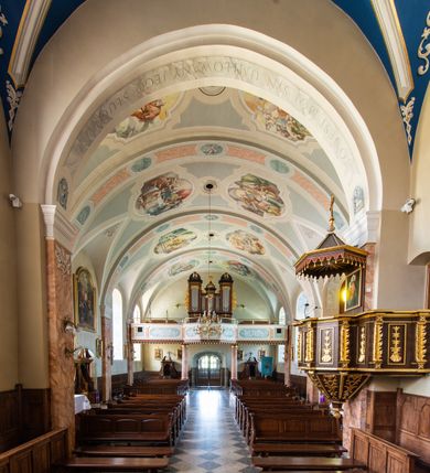 Zdjęcie nr 32: Kościół orientowany, jest budowlą murowaną z cegły i kamienia, na rzucie podłużnym. Korpus nawowy jest jednonawowy i czteroprzęsłowy. Do dwuprzęsłowego, zamkniętego trójbocznie prezbiterium od północy przylega zakrystia. Na osi kościoła, w przedłużeniu północnego przęsła jest czworoboczna, wysunięta przed lico fasady wieża. Od południa do drugiego przęsła korpusu przylega kruchta. Nawa przekryta jest sklepieniem kolebkowym z lunetami wspartymi na pilastrach, w prezbiterium sklepienie krzyżowo-żebrowe z gurtą wspartą na pilastrach. Przestrzeń prezbiterium od korpusu nawowego oddziela półkolista arkada łuku tęczowego i drewniana balustrada. Artykulację ścian na zewnątrz kościoła stanowi zespół dwuuskokowych przypór, w narożach wieży są czterouskokowe, osadzonych na niewysokim cokole. Do wnętrza prowadzą 3 otwory drzwiowe. Dwuskrzydłowe drzwi w fasadzie ujęte są kamiennym obramieniem zamkniętym łukiem koszowym z kluczem pośrodku, wspartym na gzymsie oraz 2 w północnej ścianie kaplicy bocznej. 2 prostokątne prowadzą przez kruchtę i zakrystię. Ściany korpusu nawowego i prezbiterium przeprute są prostokątnymi oknami zamkniętymi łukiem odcinkowym. Okno na zakończeniu prezbiterium jest formie półkoliście zamkniętej niszy z figurą Matki Boskiej. Kształt okien korpusu i prezbiterium został powtórzony w przyległości prezbiterium. Powyżej wejścia na osi wieży małe okienko zamknięte łukiem koszowym, wyżej nisza zamknięta ostrołukowo. W górnej partii wieży znajdują się cztery, duże, zamknięte półkoliście otwory okienne ujęte prostymi obramieniami. Szczyt wierzy obiega gzyms wieńczący z półkolistym łukiem na osi każdej ze ścian. Dach w formie hełmu z latarnią. Dach prezbiterium i korpusu dwuspadowy, kryty blachą, nad pierwszym przęsłem wieżyczka na sygnaturkę. Kruchta z dachem dwuspadowym, przyległość pulpitowym. Tynki w kolorze beżowym i białym. 