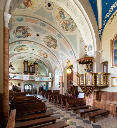 Zdjęcie nr 43: Kościół orientowany, jest budowlą murowaną z cegły i kamienia, na rzucie podłużnym. Korpus nawowy jest jednonawowy i czteroprzęsłowy. Do dwuprzęsłowego, zamkniętego trójbocznie prezbiterium od północy przylega zakrystia. Na osi kościoła, w przedłużeniu północnego przęsła jest czworoboczna, wysunięta przed lico fasady wieża. Od południa do drugiego przęsła korpusu przylega kruchta. Nawa przekryta jest sklepieniem kolebkowym z lunetami wspartymi na pilastrach, w prezbiterium sklepienie krzyżowo-żebrowe z gurtą wspartą na pilastrach. Przestrzeń prezbiterium od korpusu nawowego oddziela półkolista arkada łuku tęczowego i drewniana balustrada. Artykulację ścian na zewnątrz kościoła stanowi zespół dwuuskokowych przypór, w narożach wieży są czterouskokowe, osadzonych na niewysokim cokole. Do wnętrza prowadzą 3 otwory drzwiowe. Dwuskrzydłowe drzwi w fasadzie ujęte są kamiennym obramieniem zamkniętym łukiem koszowym z kluczem pośrodku, wspartym na gzymsie oraz 2 w północnej ścianie kaplicy bocznej. 2 prostokątne prowadzą przez kruchtę i zakrystię. Ściany korpusu nawowego i prezbiterium przeprute są prostokątnymi oknami zamkniętymi łukiem odcinkowym. Okno na zakończeniu prezbiterium jest formie półkoliście zamkniętej niszy z figurą Matki Boskiej. Kształt okien korpusu i prezbiterium został powtórzony w przyległości prezbiterium. Powyżej wejścia na osi wieży małe okienko zamknięte łukiem koszowym, wyżej nisza zamknięta ostrołukowo. W górnej partii wieży znajdują się cztery, duże, zamknięte półkoliście otwory okienne ujęte prostymi obramieniami. Szczyt wierzy obiega gzyms wieńczący z półkolistym łukiem na osi każdej ze ścian. Dach w formie hełmu z latarnią. Dach prezbiterium i korpusu dwuspadowy, kryty blachą, nad pierwszym przęsłem wieżyczka na sygnaturkę. Kruchta z dachem dwuspadowym, przyległość pulpitowym. Tynki w kolorze beżowym i białym. 