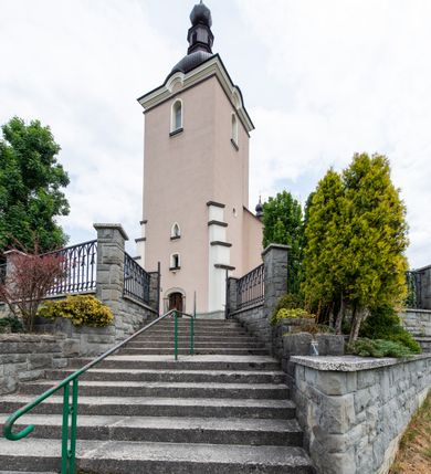 Zdjęcie nr 8: Kościół orientowany, jest budowlą murowaną z cegły i kamienia, na rzucie podłużnym. Korpus nawowy jest jednonawowy i czteroprzęsłowy. Do dwuprzęsłowego, zamkniętego trójbocznie prezbiterium od północy przylega zakrystia. Na osi kościoła, w przedłużeniu północnego przęsła jest czworoboczna, wysunięta przed lico fasady wieża. Od południa do drugiego przęsła korpusu przylega kruchta. Nawa przekryta jest sklepieniem kolebkowym z lunetami wspartymi na pilastrach, w prezbiterium sklepienie krzyżowo-żebrowe z gurtą wspartą na pilastrach. Przestrzeń prezbiterium od korpusu nawowego oddziela półkolista arkada łuku tęczowego i drewniana balustrada. Artykulację ścian na zewnątrz kościoła stanowi zespół dwuuskokowych przypór, w narożach wieży są czterouskokowe, osadzonych na niewysokim cokole. Do wnętrza prowadzą 3 otwory drzwiowe. Dwuskrzydłowe drzwi w fasadzie ujęte są kamiennym obramieniem zamkniętym łukiem koszowym z kluczem pośrodku, wspartym na gzymsie oraz 2 w północnej ścianie kaplicy bocznej. 2 prostokątne prowadzą przez kruchtę i zakrystię. Ściany korpusu nawowego i prezbiterium przeprute są prostokątnymi oknami zamkniętymi łukiem odcinkowym. Okno na zakończeniu prezbiterium jest formie półkoliście zamkniętej niszy z figurą Matki Boskiej. Kształt okien korpusu i prezbiterium został powtórzony w przyległości prezbiterium. Powyżej wejścia na osi wieży małe okienko zamknięte łukiem koszowym, wyżej nisza zamknięta ostrołukowo. W górnej partii wieży znajdują się cztery, duże, zamknięte półkoliście otwory okienne ujęte prostymi obramieniami. Szczyt wierzy obiega gzyms wieńczący z półkolistym łukiem na osi każdej ze ścian. Dach w formie hełmu z latarnią. Dach prezbiterium i korpusu dwuspadowy, kryty blachą, nad pierwszym przęsłem wieżyczka na sygnaturkę. Kruchta z dachem dwuspadowym, przyległość pulpitowym. Tynki w kolorze beżowym i białym. 