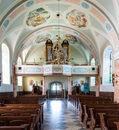 Zdjęcie nr 38: Kościół orientowany, jest budowlą murowaną z cegły i kamienia, na rzucie podłużnym. Korpus nawowy jest jednonawowy i czteroprzęsłowy. Do dwuprzęsłowego, zamkniętego trójbocznie prezbiterium od północy przylega zakrystia. Na osi kościoła, w przedłużeniu północnego przęsła jest czworoboczna, wysunięta przed lico fasady wieża. Od południa do drugiego przęsła korpusu przylega kruchta. Nawa przekryta jest sklepieniem kolebkowym z lunetami wspartymi na pilastrach, w prezbiterium sklepienie krzyżowo-żebrowe z gurtą wspartą na pilastrach. Przestrzeń prezbiterium od korpusu nawowego oddziela półkolista arkada łuku tęczowego i drewniana balustrada. Artykulację ścian na zewnątrz kościoła stanowi zespół dwuuskokowych przypór, w narożach wieży są czterouskokowe, osadzonych na niewysokim cokole. Do wnętrza prowadzą 3 otwory drzwiowe. Dwuskrzydłowe drzwi w fasadzie ujęte są kamiennym obramieniem zamkniętym łukiem koszowym z kluczem pośrodku, wspartym na gzymsie oraz 2 w północnej ścianie kaplicy bocznej. 2 prostokątne prowadzą przez kruchtę i zakrystię. Ściany korpusu nawowego i prezbiterium przeprute są prostokątnymi oknami zamkniętymi łukiem odcinkowym. Okno na zakończeniu prezbiterium jest formie półkoliście zamkniętej niszy z figurą Matki Boskiej. Kształt okien korpusu i prezbiterium został powtórzony w przyległości prezbiterium. Powyżej wejścia na osi wieży małe okienko zamknięte łukiem koszowym, wyżej nisza zamknięta ostrołukowo. W górnej partii wieży znajdują się cztery, duże, zamknięte półkoliście otwory okienne ujęte prostymi obramieniami. Szczyt wierzy obiega gzyms wieńczący z półkolistym łukiem na osi każdej ze ścian. Dach w formie hełmu z latarnią. Dach prezbiterium i korpusu dwuspadowy, kryty blachą, nad pierwszym przęsłem wieżyczka na sygnaturkę. Kruchta z dachem dwuspadowym, przyległość pulpitowym. Tynki w kolorze beżowym i białym. 
