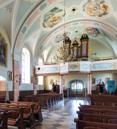 Zdjęcie nr 45: Kościół orientowany, jest budowlą murowaną z cegły i kamienia, na rzucie podłużnym. Korpus nawowy jest jednonawowy i czteroprzęsłowy. Do dwuprzęsłowego, zamkniętego trójbocznie prezbiterium od północy przylega zakrystia. Na osi kościoła, w przedłużeniu północnego przęsła jest czworoboczna, wysunięta przed lico fasady wieża. Od południa do drugiego przęsła korpusu przylega kruchta. Nawa przekryta jest sklepieniem kolebkowym z lunetami wspartymi na pilastrach, w prezbiterium sklepienie krzyżowo-żebrowe z gurtą wspartą na pilastrach. Przestrzeń prezbiterium od korpusu nawowego oddziela półkolista arkada łuku tęczowego i drewniana balustrada. Artykulację ścian na zewnątrz kościoła stanowi zespół dwuuskokowych przypór, w narożach wieży są czterouskokowe, osadzonych na niewysokim cokole. Do wnętrza prowadzą 3 otwory drzwiowe. Dwuskrzydłowe drzwi w fasadzie ujęte są kamiennym obramieniem zamkniętym łukiem koszowym z kluczem pośrodku, wspartym na gzymsie oraz 2 w północnej ścianie kaplicy bocznej. 2 prostokątne prowadzą przez kruchtę i zakrystię. Ściany korpusu nawowego i prezbiterium przeprute są prostokątnymi oknami zamkniętymi łukiem odcinkowym. Okno na zakończeniu prezbiterium jest formie półkoliście zamkniętej niszy z figurą Matki Boskiej. Kształt okien korpusu i prezbiterium został powtórzony w przyległości prezbiterium. Powyżej wejścia na osi wieży małe okienko zamknięte łukiem koszowym, wyżej nisza zamknięta ostrołukowo. W górnej partii wieży znajdują się cztery, duże, zamknięte półkoliście otwory okienne ujęte prostymi obramieniami. Szczyt wierzy obiega gzyms wieńczący z półkolistym łukiem na osi każdej ze ścian. Dach w formie hełmu z latarnią. Dach prezbiterium i korpusu dwuspadowy, kryty blachą, nad pierwszym przęsłem wieżyczka na sygnaturkę. Kruchta z dachem dwuspadowym, przyległość pulpitowym. Tynki w kolorze beżowym i białym. 