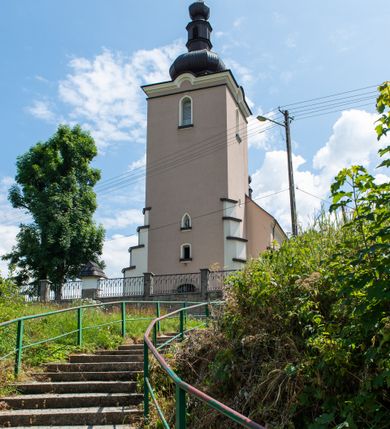 Zdjęcie nr 6: Kościół orientowany, jest budowlą murowaną z cegły i kamienia, na rzucie podłużnym. Korpus nawowy jest jednonawowy i czteroprzęsłowy. Do dwuprzęsłowego, zamkniętego trójbocznie prezbiterium od północy przylega zakrystia. Na osi kościoła, w przedłużeniu północnego przęsła jest czworoboczna, wysunięta przed lico fasady wieża. Od południa do drugiego przęsła korpusu przylega kruchta. Nawa przekryta jest sklepieniem kolebkowym z lunetami wspartymi na pilastrach, w prezbiterium sklepienie krzyżowo-żebrowe z gurtą wspartą na pilastrach. Przestrzeń prezbiterium od korpusu nawowego oddziela półkolista arkada łuku tęczowego i drewniana balustrada. Artykulację ścian na zewnątrz kościoła stanowi zespół dwuuskokowych przypór, w narożach wieży są czterouskokowe, osadzonych na niewysokim cokole. Do wnętrza prowadzą 3 otwory drzwiowe. Dwuskrzydłowe drzwi w fasadzie ujęte są kamiennym obramieniem zamkniętym łukiem koszowym z kluczem pośrodku, wspartym na gzymsie oraz 2 w północnej ścianie kaplicy bocznej. 2 prostokątne prowadzą przez kruchtę i zakrystię. Ściany korpusu nawowego i prezbiterium przeprute są prostokątnymi oknami zamkniętymi łukiem odcinkowym. Okno na zakończeniu prezbiterium jest formie półkoliście zamkniętej niszy z figurą Matki Boskiej. Kształt okien korpusu i prezbiterium został powtórzony w przyległości prezbiterium. Powyżej wejścia na osi wieży małe okienko zamknięte łukiem koszowym, wyżej nisza zamknięta ostrołukowo. W górnej partii wieży znajdują się cztery, duże, zamknięte półkoliście otwory okienne ujęte prostymi obramieniami. Szczyt wierzy obiega gzyms wieńczący z półkolistym łukiem na osi każdej ze ścian. Dach w formie hełmu z latarnią. Dach prezbiterium i korpusu dwuspadowy, kryty blachą, nad pierwszym przęsłem wieżyczka na sygnaturkę. Kruchta z dachem dwuspadowym, przyległość pulpitowym. Tynki w kolorze beżowym i białym. 