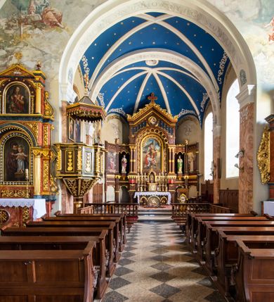 Zdjęcie nr 26: Kościół orientowany, jest budowlą murowaną z cegły i kamienia, na rzucie podłużnym. Korpus nawowy jest jednonawowy i czteroprzęsłowy. Do dwuprzęsłowego, zamkniętego trójbocznie prezbiterium od północy przylega zakrystia. Na osi kościoła, w przedłużeniu północnego przęsła jest czworoboczna, wysunięta przed lico fasady wieża. Od południa do drugiego przęsła korpusu przylega kruchta. Nawa przekryta jest sklepieniem kolebkowym z lunetami wspartymi na pilastrach, w prezbiterium sklepienie krzyżowo-żebrowe z gurtą wspartą na pilastrach. Przestrzeń prezbiterium od korpusu nawowego oddziela półkolista arkada łuku tęczowego i drewniana balustrada. Artykulację ścian na zewnątrz kościoła stanowi zespół dwuuskokowych przypór, w narożach wieży są czterouskokowe, osadzonych na niewysokim cokole. Do wnętrza prowadzą 3 otwory drzwiowe. Dwuskrzydłowe drzwi w fasadzie ujęte są kamiennym obramieniem zamkniętym łukiem koszowym z kluczem pośrodku, wspartym na gzymsie oraz 2 w północnej ścianie kaplicy bocznej. 2 prostokątne prowadzą przez kruchtę i zakrystię. Ściany korpusu nawowego i prezbiterium przeprute są prostokątnymi oknami zamkniętymi łukiem odcinkowym. Okno na zakończeniu prezbiterium jest formie półkoliście zamkniętej niszy z figurą Matki Boskiej. Kształt okien korpusu i prezbiterium został powtórzony w przyległości prezbiterium. Powyżej wejścia na osi wieży małe okienko zamknięte łukiem koszowym, wyżej nisza zamknięta ostrołukowo. W górnej partii wieży znajdują się cztery, duże, zamknięte półkoliście otwory okienne ujęte prostymi obramieniami. Szczyt wierzy obiega gzyms wieńczący z półkolistym łukiem na osi każdej ze ścian. Dach w formie hełmu z latarnią. Dach prezbiterium i korpusu dwuspadowy, kryty blachą, nad pierwszym przęsłem wieżyczka na sygnaturkę. Kruchta z dachem dwuspadowym, przyległość pulpitowym. Tynki w kolorze beżowym i białym. 