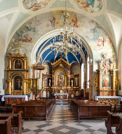 Zdjęcie nr 25: Kościół orientowany, jest budowlą murowaną z cegły i kamienia, na rzucie podłużnym. Korpus nawowy jest jednonawowy i czteroprzęsłowy. Do dwuprzęsłowego, zamkniętego trójbocznie prezbiterium od północy przylega zakrystia. Na osi kościoła, w przedłużeniu północnego przęsła jest czworoboczna, wysunięta przed lico fasady wieża. Od południa do drugiego przęsła korpusu przylega kruchta. Nawa przekryta jest sklepieniem kolebkowym z lunetami wspartymi na pilastrach, w prezbiterium sklepienie krzyżowo-żebrowe z gurtą wspartą na pilastrach. Przestrzeń prezbiterium od korpusu nawowego oddziela półkolista arkada łuku tęczowego i drewniana balustrada. Artykulację ścian na zewnątrz kościoła stanowi zespół dwuuskokowych przypór, w narożach wieży są czterouskokowe, osadzonych na niewysokim cokole. Do wnętrza prowadzą 3 otwory drzwiowe. Dwuskrzydłowe drzwi w fasadzie ujęte są kamiennym obramieniem zamkniętym łukiem koszowym z kluczem pośrodku, wspartym na gzymsie oraz 2 w północnej ścianie kaplicy bocznej. 2 prostokątne prowadzą przez kruchtę i zakrystię. Ściany korpusu nawowego i prezbiterium przeprute są prostokątnymi oknami zamkniętymi łukiem odcinkowym. Okno na zakończeniu prezbiterium jest formie półkoliście zamkniętej niszy z figurą Matki Boskiej. Kształt okien korpusu i prezbiterium został powtórzony w przyległości prezbiterium. Powyżej wejścia na osi wieży małe okienko zamknięte łukiem koszowym, wyżej nisza zamknięta ostrołukowo. W górnej partii wieży znajdują się cztery, duże, zamknięte półkoliście otwory okienne ujęte prostymi obramieniami. Szczyt wierzy obiega gzyms wieńczący z półkolistym łukiem na osi każdej ze ścian. Dach w formie hełmu z latarnią. Dach prezbiterium i korpusu dwuspadowy, kryty blachą, nad pierwszym przęsłem wieżyczka na sygnaturkę. Kruchta z dachem dwuspadowym, przyległość pulpitowym. Tynki w kolorze beżowym i białym. 