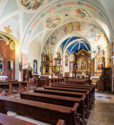 Zdjęcie nr 30: Kościół orientowany, jest budowlą murowaną z cegły i kamienia, na rzucie podłużnym. Korpus nawowy jest jednonawowy i czteroprzęsłowy. Do dwuprzęsłowego, zamkniętego trójbocznie prezbiterium od północy przylega zakrystia. Na osi kościoła, w przedłużeniu północnego przęsła jest czworoboczna, wysunięta przed lico fasady wieża. Od południa do drugiego przęsła korpusu przylega kruchta. Nawa przekryta jest sklepieniem kolebkowym z lunetami wspartymi na pilastrach, w prezbiterium sklepienie krzyżowo-żebrowe z gurtą wspartą na pilastrach. Przestrzeń prezbiterium od korpusu nawowego oddziela półkolista arkada łuku tęczowego i drewniana balustrada. Artykulację ścian na zewnątrz kościoła stanowi zespół dwuuskokowych przypór, w narożach wieży są czterouskokowe, osadzonych na niewysokim cokole. Do wnętrza prowadzą 3 otwory drzwiowe. Dwuskrzydłowe drzwi w fasadzie ujęte są kamiennym obramieniem zamkniętym łukiem koszowym z kluczem pośrodku, wspartym na gzymsie oraz 2 w północnej ścianie kaplicy bocznej. 2 prostokątne prowadzą przez kruchtę i zakrystię. Ściany korpusu nawowego i prezbiterium przeprute są prostokątnymi oknami zamkniętymi łukiem odcinkowym. Okno na zakończeniu prezbiterium jest formie półkoliście zamkniętej niszy z figurą Matki Boskiej. Kształt okien korpusu i prezbiterium został powtórzony w przyległości prezbiterium. Powyżej wejścia na osi wieży małe okienko zamknięte łukiem koszowym, wyżej nisza zamknięta ostrołukowo. W górnej partii wieży znajdują się cztery, duże, zamknięte półkoliście otwory okienne ujęte prostymi obramieniami. Szczyt wierzy obiega gzyms wieńczący z półkolistym łukiem na osi każdej ze ścian. Dach w formie hełmu z latarnią. Dach prezbiterium i korpusu dwuspadowy, kryty blachą, nad pierwszym przęsłem wieżyczka na sygnaturkę. Kruchta z dachem dwuspadowym, przyległość pulpitowym. Tynki w kolorze beżowym i białym. 