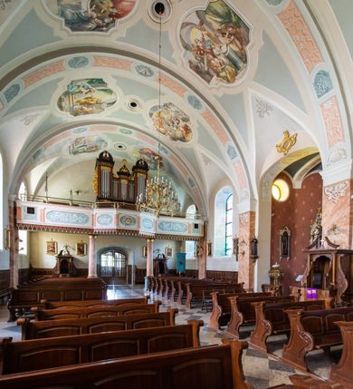 Zdjęcie nr 48: Kościół orientowany, jest budowlą murowaną z cegły i kamienia, na rzucie podłużnym. Korpus nawowy jest jednonawowy i czteroprzęsłowy. Do dwuprzęsłowego, zamkniętego trójbocznie prezbiterium od północy przylega zakrystia. Na osi kościoła, w przedłużeniu północnego przęsła jest czworoboczna, wysunięta przed lico fasady wieża. Od południa do drugiego przęsła korpusu przylega kruchta. Nawa przekryta jest sklepieniem kolebkowym z lunetami wspartymi na pilastrach, w prezbiterium sklepienie krzyżowo-żebrowe z gurtą wspartą na pilastrach. Przestrzeń prezbiterium od korpusu nawowego oddziela półkolista arkada łuku tęczowego i drewniana balustrada. Artykulację ścian na zewnątrz kościoła stanowi zespół dwuuskokowych przypór, w narożach wieży są czterouskokowe, osadzonych na niewysokim cokole. Do wnętrza prowadzą 3 otwory drzwiowe. Dwuskrzydłowe drzwi w fasadzie ujęte są kamiennym obramieniem zamkniętym łukiem koszowym z kluczem pośrodku, wspartym na gzymsie oraz 2 w północnej ścianie kaplicy bocznej. 2 prostokątne prowadzą przez kruchtę i zakrystię. Ściany korpusu nawowego i prezbiterium przeprute są prostokątnymi oknami zamkniętymi łukiem odcinkowym. Okno na zakończeniu prezbiterium jest formie półkoliście zamkniętej niszy z figurą Matki Boskiej. Kształt okien korpusu i prezbiterium został powtórzony w przyległości prezbiterium. Powyżej wejścia na osi wieży małe okienko zamknięte łukiem koszowym, wyżej nisza zamknięta ostrołukowo. W górnej partii wieży znajdują się cztery, duże, zamknięte półkoliście otwory okienne ujęte prostymi obramieniami. Szczyt wierzy obiega gzyms wieńczący z półkolistym łukiem na osi każdej ze ścian. Dach w formie hełmu z latarnią. Dach prezbiterium i korpusu dwuspadowy, kryty blachą, nad pierwszym przęsłem wieżyczka na sygnaturkę. Kruchta z dachem dwuspadowym, przyległość pulpitowym. Tynki w kolorze beżowym i białym. 