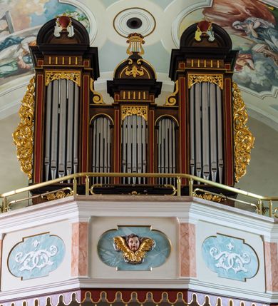 Zdjęcie nr 49: Kościół orientowany, jest budowlą murowaną z cegły i kamienia, na rzucie podłużnym. Korpus nawowy jest jednonawowy i czteroprzęsłowy. Do dwuprzęsłowego, zamkniętego trójbocznie prezbiterium od północy przylega zakrystia. Na osi kościoła, w przedłużeniu północnego przęsła jest czworoboczna, wysunięta przed lico fasady wieża. Od południa do drugiego przęsła korpusu przylega kruchta. Nawa przekryta jest sklepieniem kolebkowym z lunetami wspartymi na pilastrach, w prezbiterium sklepienie krzyżowo-żebrowe z gurtą wspartą na pilastrach. Przestrzeń prezbiterium od korpusu nawowego oddziela półkolista arkada łuku tęczowego i drewniana balustrada. Artykulację ścian na zewnątrz kościoła stanowi zespół dwuuskokowych przypór, w narożach wieży są czterouskokowe, osadzonych na niewysokim cokole. Do wnętrza prowadzą 3 otwory drzwiowe. Dwuskrzydłowe drzwi w fasadzie ujęte są kamiennym obramieniem zamkniętym łukiem koszowym z kluczem pośrodku, wspartym na gzymsie oraz 2 w północnej ścianie kaplicy bocznej. 2 prostokątne prowadzą przez kruchtę i zakrystię. Ściany korpusu nawowego i prezbiterium przeprute są prostokątnymi oknami zamkniętymi łukiem odcinkowym. Okno na zakończeniu prezbiterium jest formie półkoliście zamkniętej niszy z figurą Matki Boskiej. Kształt okien korpusu i prezbiterium został powtórzony w przyległości prezbiterium. Powyżej wejścia na osi wieży małe okienko zamknięte łukiem koszowym, wyżej nisza zamknięta ostrołukowo. W górnej partii wieży znajdują się cztery, duże, zamknięte półkoliście otwory okienne ujęte prostymi obramieniami. Szczyt wierzy obiega gzyms wieńczący z półkolistym łukiem na osi każdej ze ścian. Dach w formie hełmu z latarnią. Dach prezbiterium i korpusu dwuspadowy, kryty blachą, nad pierwszym przęsłem wieżyczka na sygnaturkę. Kruchta z dachem dwuspadowym, przyległość pulpitowym. Tynki w kolorze beżowym i białym. 