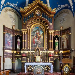 Zdjęcie nr 1: Ołtarz architektoniczny, jednokondygnacyjny, pięcioosiowy, na dwustrefowym cokole z bramkami w jego partii. Ołtarz prostopadłościenny, murowany, w drewnianej obudowie. Antepedium podzielone na trzy pola czterema pilastrami; w środkowym płaskorzeźbione serce ujęte krzyżem i kotwicą oraz kwiatami, w bocznych dekoracja roślinna. 
Tabernakulum w formie drewnianej skrzynki na planie prostokąta o ściętych przednich narożach, na profilowanym cokole, zamknięte gzymsem. Ścianka frontowa metalowa z drzwiczkami w formie stojącego prostokąta zamkniętego łukiem półkolistym z aplikowanym krzyżem z gorejącym sercem w glorii oraz winnym gronem i kłosami zbóż u spodu. Powyżej w przyłuczach aplikowana dekoracja w postaci winnego grona i kłosów zboża. Naroża i ścianki boczne dekorowane płycinami z płaskorzeźbionymi kwiatami i aplikowanymi metalowymi płytkami z kłosami zbóż. Na tabernakulum tron wystawienia w postaci baldachimu na czterech kolumienkach ze ścianką tylną z płaskorzeźbioną glorią promienistą. Baldachim o łukach ostrych, na froncie trójlistnym, z podwieszonymi wspornikami; całość zakończona krzyżem. 
Oś środkowa retabulum wyższa i szersza od pozostałych, ujęta dwiema parami stylizowanych kolumn dźwigającym archiwoltę oraz stylizowaną wimpergę, w której polu znajduje się fryz arkadkowy i medalion z płaskorzeźbioną Madonną z Dzieciątkiem (według Rafaela Santi), całość zamknięta trójkątnym gzymsem nadwieszonym, dekorowanym stylizowanym akantem, z krzyżem wieńczącym. W polu centralnym nisza w formie stojącego prostokąta zamkniętego łukiem półkolistym z wymiennymi figurami Matki Boskiej i Najświętszego Serca Jezusa, ujęta profilowaną ramą oraz pasem ornamentu roślinnego, na zasuwie wizerunek św. Marcina z Tours dzielącego się płaszczem z żebrakiem. Nisze boczne wydzielone wąskimi kolumienkami dźwigającymi niepełne belkowanie z dekoracją geometryczną i roślinną. W niszach środkowych na cokołach figury św. Piotra i św. Pawła; na osiach skrajnych malowane na desce przedstawienia św. Marcina jako mnicha po lewej stronie i św. Marcina jako biskupa po prawej. W dolnej partii strefy cokołu, na osiach wewnętrznych bramki w formie przejść; na skrajnych osiach siedziska. W partii drugiej strefy cokołu krenelaż, ornament ze stylizowanych lilii heraldycznych i płaskorzeźbiona dekoracja roślinna. Struktura w kolorze naturalnego drewna, z polichromowanymi na niebiesko i czerwono akcentami; ornamentyka i detale architektoniczne złocone.
