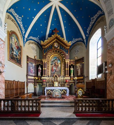 Zdjęcie nr 2: Ołtarz architektoniczny, jednokondygnacyjny, pięcioosiowy, na dwustrefowym cokole z bramkami w jego partii. Ołtarz prostopadłościenny, murowany, w drewnianej obudowie. Antepedium podzielone na trzy pola czterema pilastrami; w środkowym płaskorzeźbione serce ujęte krzyżem i kotwicą oraz kwiatami, w bocznych dekoracja roślinna. 
Tabernakulum w formie drewnianej skrzynki na planie prostokąta o ściętych przednich narożach, na profilowanym cokole, zamknięte gzymsem. Ścianka frontowa metalowa z drzwiczkami w formie stojącego prostokąta zamkniętego łukiem półkolistym z aplikowanym krzyżem z gorejącym sercem w glorii oraz winnym gronem i kłosami zbóż u spodu. Powyżej w przyłuczach aplikowana dekoracja w postaci winnego grona i kłosów zboża. Naroża i ścianki boczne dekorowane płycinami z płaskorzeźbionymi kwiatami i aplikowanymi metalowymi płytkami z kłosami zbóż. Na tabernakulum tron wystawienia w postaci baldachimu na czterech kolumienkach ze ścianką tylną z płaskorzeźbioną glorią promienistą. Baldachim o łukach ostrych, na froncie trójlistnym, z podwieszonymi wspornikami; całość zakończona krzyżem. 
Oś środkowa retabulum wyższa i szersza od pozostałych, ujęta dwiema parami stylizowanych kolumn dźwigającym archiwoltę oraz stylizowaną wimpergę, w której polu znajduje się fryz arkadkowy i medalion z płaskorzeźbioną Madonną z Dzieciątkiem (według Rafaela Santi), całość zamknięta trójkątnym gzymsem nadwieszonym, dekorowanym stylizowanym akantem, z krzyżem wieńczącym. W polu centralnym nisza w formie stojącego prostokąta zamkniętego łukiem półkolistym z wymiennymi figurami Matki Boskiej i Najświętszego Serca Jezusa, ujęta profilowaną ramą oraz pasem ornamentu roślinnego, na zasuwie wizerunek św. Marcina z Tours dzielącego się płaszczem z żebrakiem. Nisze boczne wydzielone wąskimi kolumienkami dźwigającymi niepełne belkowanie z dekoracją geometryczną i roślinną. W niszach środkowych na cokołach figury św. Piotra i św. Pawła; na osiach skrajnych malowane na desce przedstawienia św. Marcina jako mnicha po lewej stronie i św. Marcina jako biskupa po prawej. W dolnej partii strefy cokołu, na osiach wewnętrznych bramki w formie przejść; na skrajnych osiach siedziska. W partii drugiej strefy cokołu krenelaż, ornament ze stylizowanych lilii heraldycznych i płaskorzeźbiona dekoracja roślinna. Struktura w kolorze naturalnego drewna, z polichromowanymi na niebiesko i czerwono akcentami; ornamentyka i detale architektoniczne złocone.
