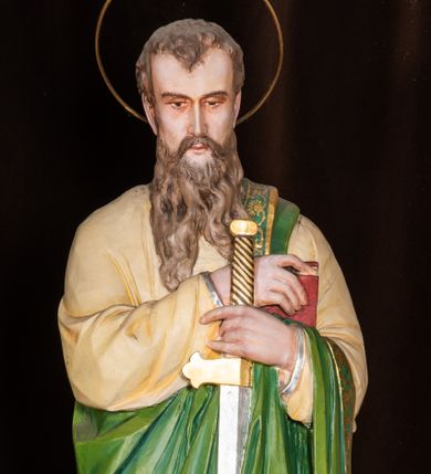 Zdjęcie nr 1: Całopostaciowa, pełnoplastyczna figura św. Pawła stojącego w lekkim kontrapoście na niewysokiej, ośmiobocznej podstawie, zwróconego na wprost. Nieznacznie pochyloną głowę, o lekkich zakolach i krótkich włosach, charakteryzuje pociągła twarz o delikatnych, miękko modelowanych rysach i długim, jasnobrązowym zaroście, ze wzrokiem skierowanym w dół. Święty ubrany jest w beżową suknię i narzucony na lewe ramię i przewieszony przez rękę jasnozielony płaszcz ze złoconą bordiurą. W złożonych z przodu, przy talii rękach trzyma miecz skierowany ostrzem w dół – w prawej i księgę w czerwonej oprawie – w lewej. Głowę okala złocona aureola.   