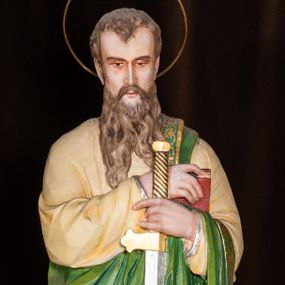 Zdjęcie nr 1: Całopostaciowa, pełnoplastyczna figura św. Pawła stojącego w lekkim kontrapoście na niewysokiej, ośmiobocznej podstawie, zwróconego na wprost. Nieznacznie pochyloną głowę, o lekkich zakolach i krótkich włosach, charakteryzuje pociągła twarz o delikatnych, miękko modelowanych rysach i długim, jasnobrązowym zaroście, ze wzrokiem skierowanym w dół. Święty ubrany jest w beżową suknię i narzucony na lewe ramię i przewieszony przez rękę jasnozielony płaszcz ze złoconą bordiurą. W złożonych z przodu, przy talii rękach trzyma miecz skierowany ostrzem w dół – w prawej i księgę w czerwonej oprawie – w lewej. Głowę okala złocona aureola.   