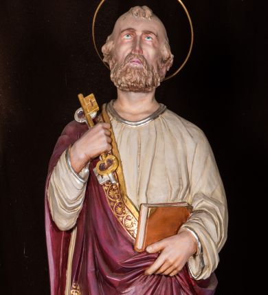 Zdjęcie nr 1: Całopostaciowa, pełnoplastyczna figura św. Piotra stojącego w kontrapoście na niewysokiej, ośmiobocznej podstawie, zwróconego na wprost. Odchyloną lekko do tyłu głowę, o wydatnych zakolach i kępkach włosów po bokach i nad czołem, charakteryzuje pociągła twarz o delikatnych rysach i krótkim, jasnobrązowym zaroście, ze wzrokiem skierowanym do góry. Święty ubrany jest w beżową suknię i przewieszony przez prawe ramię bordowy płaszcz ze złoconą bordiurą. W podniesionej i wspartej na ramieniu prawej ręce ma parę złoconych i srebrzonych kluczy, lewą podtrzymuje połę płaszcza i zamkniętą księgę w czerwonej oprawie. Głowę okala złocona aureola.   
