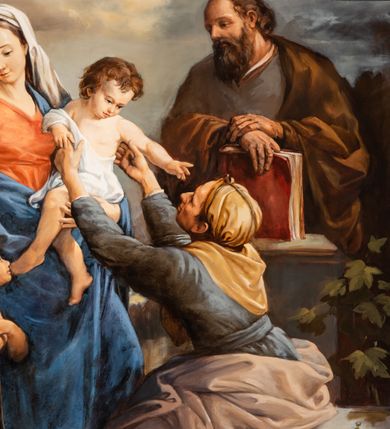 Zdjęcie nr 5: Obraz w kształcie zbliżonym do kwadratu zamkniętego półkolistym łukiem nadwieszonym, ujęty dekoracyjną ramą z motywem złocono-srebrzonego astragalu, marmoryzacji i złoconej listwy w kształcie półwałka. Wielofiguralna kompozycja przedstawia Świętą Rodzinę ze św. Anną i małym św. Janem Chrzcicielem. Pośrodku ukazana jest stojąca postać Marii zwróconej w trzech czwartych w lewo i spoglądającej w dół w prawo. Owalną twarz charakteryzuje promienna cera o delikatnych, młodzieńczych rysach. Maria ubrana jest w czerwoną suknię i niebieski płaszcz, na głowie ma białą, opadającą na ramiona chustę. Lewą rękę podtrzymuje Dzieciątko Jezus, prawą przygarnia do siebie zwróconego profilem w lewo Jana Chrzciciela. Ukazany w wykroku św. Jan jest lekko pochylony w kierunku Marii. Zaokrągloną twarz charakteryzują delikatne, dziecięce rysy. Włosy ma krótkie, kręcone. Nagą sylwetkę przesłania krótka, zarzucona na lewe ramię skóra zwierzęca. Złożonymi na piersiach rękami podtrzymuje krzyż na długim drzewcu z banderolą. U stóp leży baranek. Jan spogląda w kierunku odwracającego się w lewo Dzieciątka. Pochyloną głowę charakteryzują owalna twarz o drobnych rysach i krótkie, brązowe włosy. Nagą sylwetkę osłania biała szata. Jezus wyciąga ręce w kierunku siedzącej na kamiennym postumencie św. Anny. Zwrócona profilem w prawo kobieta pochyla się nieco do przodu, odchylając do tyłu głowę. Widoczna częściowo twarz o cechach kobiety w podeszłym wieku. Święta ubrana jest w szaroniebieską, przewiązaną w pasie suknię, żółtą, związaną nad czołem chustę opadającą na plecy oraz zsuwający się z bioder popielaty płaszcz. Stopy są bose. Ręce wyciąga do góry, w kierunku Jezusa. W tle, za św. Anną stoi św. Józef w trzech czwartych zwrócony w prawo. Lekko łysiejącą głowę, o brązowych włosach charakteryzuje pociągła twarz z długim, ciemnobrązowym zarostem. Święty ubrany jest w szarobrązową suknię i narzucony na ramiona brązowy płaszcz. Lewą dłoń wspiera na nadgarstku prawej ręki, którą podtrzymuje wspartą na kamiennym postumencie księgę w czerwonej oprawie. W głębi, po lewej stronie kompozycji widoczna jest postać stojącego anioła o przechylonej w lewo głowie i rękach złożonych w geście modlitwy. Ubrany jest w długą, rozwianą niebiesko-szarą szatę. W górnej partii obrazu, pośród pokrywających niebo obłoków jest anioł i para uskrzydlonych główek anielskich. Tło sceny stanowi pejzaż o obniżonej linii horyzontu, kompozycję dopełnia widoczna po prawej stronie obrazu roślinność.         
Na ramie tabliczka z napisem „FUNDATOR / GRAŻYNA I JAN WÓJCIAK” .