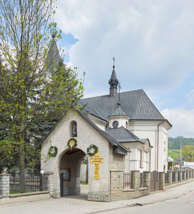 Zdjęcie nr 6: Kościół jest usytuowany pośrodku wsi Waksmund, na północ od głównej drogi z Łopusznej do Nowego Targu. Teren wokół niego jest otoczony żeliwnym płotem na kamiennej podmurówce. Na plac kościelny, od strony północno-wschodniej prowadzi murowana, otynkowana brama, nakryta dwuspadowym daszkiem z rzeźbą św. Michała Archanioła umieszczoną we wnęce nad arkadą od strony zewnętrznej.

Kościół jest orientowany. Bryłę świątyni tworzy trójnawowy korpus (przed rozbudową jednonawowy) z pseudotranseptem, węższe prezbiterium zakończone trójbocznie i wieża od zachodu. Główne wejście do świątyni prowadzi od strony zachodniej poprzez obszerną kruchtę rozbudowaną na szerokość całego kościoła z trójprzęsłową arkadą pośrodku. Osobne wejścia znajdują się od strony południowej poprzez niewielki przedsionek kaplicy oraz od strony północnej poprzez drzwi do zakrystii. Kaplica i zakrystia umieszczone są na zakończeniu naw bocznych od strony wschodniej. Wnętrze świątyni artykułowane jest masywnymi filarami, ustawionymi na styku nawy głównej z nawami bocznymi, które wspierają sklepienia krzyżowo-żebrowe. Nawę główną od prezbiterium, a także od ramion pseudotranseptu oddzielają półkoliście zakończone arkady. Na zakończeniu naw od strony zachodniej, znajdują się chóry muzyczne, głęboko wysunięte ku środkowi kościoła, z wybrzuszoną częścią środkową; w nawie głównej chór wsparty jest na parze kolumn. Nawy są oświetlone umieszczonymi w południowych i północnych ścianach prostokątnymi otworami okiennymi, zamkniętymi półkoliście (większymi na zakończeniu ramion pseudotraseptu i mniejszymi w nawach bocznych oraz w kaplicy i zakrystii). Okna w pseudotransepcie oraz jedno w kaplicy przeszklone są witrażami. Dodatkowe, pojedyncze okrągłe otwory okienne znajdują się w lukarnach oraz na ścianie wschodniej prezbiterium.

W zewnętrznej elewacji kościoła widoczny jest niewysoki, kamienny cokół, wykonany z regularnych ciosów kamienia. Elewacje ścian artykułowane są pionowymi lizenami oraz zakończone są niepełnym belkowaniem z profilowanymi gzymsami, opasującym cały budynek. Wieża jest trójkondygnacyjna, wtopiona w bryłę kościoła, na planie kwadratu. W partii drugiej kondygnacji naroża flankowane są lizenami, znajduje się tam również niewielkie okno od strony zachodniej; trzecia o ściętych narożach, a każda ze ścian przepruta jest otworami oraz dekorowana tarczami zegarowymi. 

Nawa główna z prezbiterium oraz pseduotransept nakryte są dwuspadowymi dachami z ocynkowanej blachy, a nad nawami bocznymi i kruchtą z przodu kościoła położone są dachy wielospadowe z lukarnami. Wieża nakryta jest ośmiobocznym, smukłym dachem wieżowym, zakończonym żeliwnym krzyżem, osadzonym na kuli. Nad kaplicą południową wznosi się niewielka wieżyczka z okrągłymi, małymi okienkami, nakryta ośmiospadowym niewysokim dachem wieżowym z krzyżem w zwieńczeniu, a na skrzyżowaniu nawy głównej z pseudotranseptem umieszczona jest niewielka wieżyczka na sygnaturkę, nakryta dachem wieżowym, zakończonym krzyżem.

