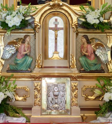 Zdjęcie nr 9: Ołtarz drewniany, zbliżony do prostopadłościanu, zwężający się ku dołowi, zakończony profilowanym gzymsem. Antependium dekorowane płycinami. Mensa drewniana. 

Tabernakulum połączone z tronem wystawienia, trójosiowe, ustawione na wysokim prostopadłościennym cokole, przed który wysunięta jest prostopadłościenna skrzynka tabernakulum. Tabernakulum ustawione na niskim, profilowanym cokole, flankowane pilastrami z płaskorzeźbionym winnym gronem, zamknięte od góry profilowanym gzymsem. Drzwiczki metalowe, groszkowane z aplikowanym kielichem z Hostią w glorii, ujęte esownicami. Tron wystawienia ustawiony nad tabernakulum w formie skrzynki zamkniętej półkoliście dwoma antytetycznymi esownicami, całość zwieńczona figurką baranka leżącego na księdze; nisza obrotowa, z jednej strony wypukła z płaskorzeźbionym przedstawieniem krucyfiksu. Tron flankują dwie ścianki stanowiące tło dla dwóch figur adorujących, czyli klęczących na cokołach aniołów. 

Nastawa ołtarzowa architektoniczna, trójosiowa z bramkami, jednokondygnacyjna ze zwieńczeniem, ustawiona na wysokim, dwustrefowym cokole. Osie wydzielone dwiema parami pilastrów i stojących przed nimi smukłych kolumn o stylizowanych kapitelach kompozytowych i skręconych trzonach na wysokości 2/5. Podpory dźwigają pełne belkowanie wyłamane na ich osi, przyjmujące nad polem środkowym kształt łuku segmentowego; na belkowaniu dwie figury aniołów dmących w trąby na ornamentalnych konsolach. W polu środkowym głęboka nisza ujęta profilowaną ramą w formie stojącego prostokąta, zamkniętego łukiem półkolistym nadwieszonym z figurą Matki Boskiej z Lourdes, na osiach bocznych na ornamentalnych konsolach figury św. Katarzyny po lewej stronie i św. Barbary po prawej stronie. Zwieńczenie w formie stojącego prostokąta zamkniętego półkoliście dwiema antytetycznie ustawionymi wolutami oraz krzyżem na szczycie; boki zwieńczenia ujęte spływami wolutowymi. W polu zwieńczenia obraz z przedstawieniem Trójcy Świętej ujęty profilowaną ramą w formie stojącego prostokąta zamkniętego łukiem półkolistym nadwieszonym oraz stylizowaną archiwoltą. Całość zamknięta dwiema wolutami z liści stylizowanego akantu oraz krzyżykiem. Bramki w formie drzwiczek na wysokości cokołu ołtarza, zamkniętych ukośnie z dekoracją ornamentalną wzdłuż brzegu. Po bokach bramek dwa cokoły wsparte na kolumnach, na których ustawione są rzeźby: św. Piotra po lewej stronie i św. Pawła po drugiej. 

Fryz dekorowany palmetami ujętymi ornamentem roślinnym; nad łukiem niszy środkowej muszla i ornament roślinny; ponad belkowaniem uskrzydlona główka anielska. Na belkowaniu, na osiach skrajnych stylizowane wazony. Zwieńczenie ujęte festonami utworzonymi z róż, kampanuli i wici roślinnej. Struktura polichromowana w kolorze beżowym, jasnoróżowymi i bordowymi akcentami; kolumny, profile i ornamentyka złocone. Po prawej stronie ołtarza sygnatura: &quot;G(RZEGORZ) F(RANCISZEK) BEŁTOWSKI / Nowy Targ / 1909&quot;.
