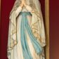 Zdjęcie nr 1: Rzeźba pełnoplastyczna, ustawiona na niskim postumencie z przedstawieniem Matki Boskiej z Lourdes. Maria ukazana frontalnie, w postawie stojącej, w delikatnym kontrapoście, z lewą nogą ugiętą w kolanie i z rękami złożonymi w geście modlitwy. Matka Boska ubrana jest w białą suknię ze złotą lamówką u szyi, przewiązaną w talii błękitną szarfą oraz biały płaszcz założony na głowę i spływający delikatnymi falami wzdłuż całej postaci, na brzegach obwiedziony złotą i dekoracyjną bordiurą. Twarz owalna z długim i wąskim nosem, z wyraźnie zaznaczonym podbródkiem oraz dużymi i niebieskimi oczami; na głowie korona w typie otwartym. Polichromia w odsłoniętych partiach ciała naturalistyczna.


