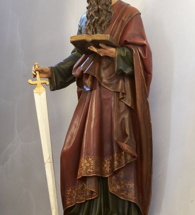 Zdjęcie nr 2: Rzeźba pełnoplastyczna ustawiona na niskim, prostokątnym cokole o ściętych narożach. Święty Paweł ukazany frontalnie, w pozycji stojącej, w delikatnym kontrapoście, z prawą nogą ugiętą w kolanie. W prawej dłoni trzyma miecz, skierowany ostrzem w dół, a w lewej otwartą księgę. Ubrany w jest długą, zieloną suknię z długimi rękawami oraz czerwony płaszcz  zarzucony na lewe ramię, z drugim końcem przewieszonym pod prawą ręką, zdobiony na obrzeżach stylizowaną wicią roślinną; na stopach ma założone ciemnobrązowe sandały. Twarz z długim i orlim nosem, wzrokiem skierowanym na księgę, okolona długą i ciemnobrązową brodą. Włosy średniej długości, ciemnobrązowe, opadające do tyłu na plecy. Polichromia naturalistyczna w odsłoniętych partiach ciała, detale złocone i srebrzone.




