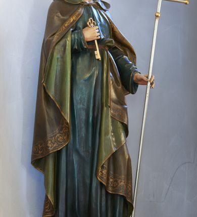 Zdjęcie nr 2: Rzeźba św. Piotra pełnoplastyczna, ustawiona na niskim cokole o ściętych narożach. Święty ukazany jest frontalnie, w pozycji stojącej, w delikatnym kontrapoście z lewą nogą ugiętą w kolanie. W prawej ręce, ugietej w łokciu, trzyma złoty klucz, a w lewej dłoni srebrzony krzyż papieski (ferulę) ze złoconymi gałkami na zakończeniach ramion. Ubrany jest w długą, ciemnozieloną suknię z długimi rękawami, przepasaną w talii paskiem oraz oliwkowozielony płaszcz z kapturem i jasnozieloną podszewką, spięty pod szyją; na stopach ma ciemnobrązowe sandały. Płaszcz zdobiony jest na brzegu szeroką bordiurą w formie stylizowanej wici roślinnej. Twarz podłużna z długim i prostym nosem, wzrokiem skierowanym przed siebie, okolona ciemnobrązową brodą. Na głowie zaznaczona łysina z kępką włosów nad czołem i lokami zawiniętymi po bokach głowy. Polichromia naturalistyczna w odsłoniętych partiach ciała, detale złocone.

