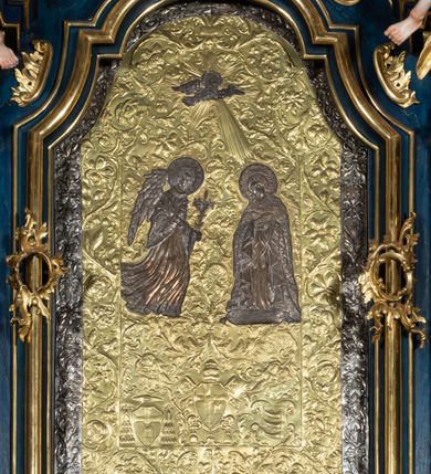 Zdjęcie nr 29: Nastawa architektoniczna, jednoosiowa, jednokondygnacyjna ze zwieńczeniem, ustawiona na wysokim cokole. Ołtarz drewniany, prostopadłościenny, o falistych bokach, mensa drewniana z marmurowym portatylem w drewnianej obudowie. Antepedium ujęte szeroką ramą dekorowaną płaskorzeźbionym motywem wieńca przepasanego wstęgą, w polu medalion z monogramem Marii ujęty wychodzącymi spod jego spodu wiązankami utworzonymi z suchego, wijącego się akantu z karbowaną wstęgą. Nastawa ujęta dwiema parami pilastrów, wewnętrzną z wolutowymi wspornikami w połowie wysokości trzonów oraz zewnętrzną parą o trzonach w formie spływów wolutowych przechodzących w silnie wysunięte do przodu partie cokołu, na których znajdują się postumenty dla figur aniołów. Podpory dźwigają niepełne belkowanie wyłamane na ich osi, nad polem środkowym wyłącznie gzyms przyjmujący kształt łuku półkolistego. Na belkowaniu fragmenty przerwanego, falistego przyczółka oraz para aniołów z kartuszami. W polu środkowym wnęka w formie stojącego prostokąta zamkniętego łukiem segmentowym nadwieszonym z uskokiem, w profilowanej ramie z mniejszym obrazem Matki Boskiej z Dzieciątkiem w kształcie stojącego prostokąta. Poniżej gablota na wota w formie leżącego prostokąta ujęta profilowaną ramą. Kondygnacja flankowana uszami utworzonymi z rocaille&#039;u. Zwieńczenie w formie zbliżonej do kwadratu o wklęsłych bokach przechodzących w woluty, na których siedzą putta, zamknięte fragmentem falistego gzymsu wyłamanego po bokach, na nim rokokowy kartusz z monogramem IHS w polu, flankowany rocaille&#039;em. W polu zwieńczenia rzeźba gołębicy Ducha Świętego w glorii promienistej i otoku z obłoków, w towarzystwie czterech uskrzydlonych główek anielskich. Wszystkie pilastry oraz łuki dekorowane elementami rocaille&#039;u. Struktura w całości polichromowana na sposób imitujący marmoryzację w kolorze niebieskim, ornamentyka i profile złocone, detal srebrzony. 
Wewnątrz skrzyni ołtarzowej napisy „MALOWAŁ LUDWIK WÓJCIK Z KRAKOWA 2 / XI 1914”; „LUDWIK WÓJCIK”; „MALOWALI STOPY”; „23.02.1994 / KONSERWOWALI / KAZIMIERZ PATEJUK / EWA I JERZY SUCHWAŁKO / Z WARSZAWY / PROBOSZCZOWAŁ / KS. BOLESŁAW WAWAK”. 