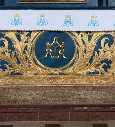 Zdjęcie nr 19: Nastawa architektoniczna, jednoosiowa, jednokondygnacyjna ze zwieńczeniem, ustawiona na wysokim cokole. Ołtarz drewniany, prostopadłościenny, o falistych bokach, mensa drewniana z marmurowym portatylem w drewnianej obudowie. Antepedium ujęte szeroką ramą dekorowaną płaskorzeźbionym motywem wieńca przepasanego wstęgą, w polu medalion z monogramem Marii ujęty wychodzącymi spod jego spodu wiązankami utworzonymi z suchego, wijącego się akantu z karbowaną wstęgą. Nastawa ujęta dwiema parami pilastrów, wewnętrzną z wolutowymi wspornikami w połowie wysokości trzonów oraz zewnętrzną parą o trzonach w formie spływów wolutowych przechodzących w silnie wysunięte do przodu partie cokołu, na których znajdują się postumenty dla figur aniołów. Podpory dźwigają niepełne belkowanie wyłamane na ich osi, nad polem środkowym wyłącznie gzyms przyjmujący kształt łuku półkolistego. Na belkowaniu fragmenty przerwanego, falistego przyczółka oraz para aniołów z kartuszami. W polu środkowym wnęka w formie stojącego prostokąta zamkniętego łukiem segmentowym nadwieszonym z uskokiem, w profilowanej ramie z mniejszym obrazem Matki Boskiej z Dzieciątkiem w kształcie stojącego prostokąta. Poniżej gablota na wota w formie leżącego prostokąta ujęta profilowaną ramą. Kondygnacja flankowana uszami utworzonymi z rocaille'u. Zwieńczenie w formie zbliżonej do kwadratu o wklęsłych bokach przechodzących w woluty, na których siedzą putta, zamknięte fragmentem falistego gzymsu wyłamanego po bokach, na nim rokokowy kartusz z monogramem IHS w polu, flankowany rocaille'em. W polu zwieńczenia rzeźba gołębicy Ducha Świętego w glorii promienistej i otoku z obłoków, w towarzystwie czterech uskrzydlonych główek anielskich. Wszystkie pilastry oraz łuki dekorowane elementami rocaille'u. Struktura w całości polichromowana na sposób imitujący marmoryzację w kolorze niebieskim, ornamentyka i profile złocone, detal srebrzony. 
Wewnątrz skrzyni ołtarzowej napisy „MALOWAŁ LUDWIK WÓJCIK Z KRAKOWA 2 / XI 1914”; „LUDWIK WÓJCIK”; „MALOWALI STOPY”; „23.02.1994 / KONSERWOWALI / KAZIMIERZ PATEJUK / EWA I JERZY SUCHWAŁKO / Z WARSZAWY / PROBOSZCZOWAŁ / KS. BOLESŁAW WAWAK”. 