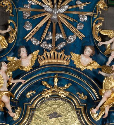 Zdjęcie nr 10: Nastawa architektoniczna, jednoosiowa, jednokondygnacyjna ze zwieńczeniem, ustawiona na wysokim cokole. Ołtarz drewniany, prostopadłościenny, o falistych bokach, mensa drewniana z marmurowym portatylem w drewnianej obudowie. Antepedium ujęte szeroką ramą dekorowaną płaskorzeźbionym motywem wieńca przepasanego wstęgą, w polu medalion z monogramem Marii ujęty wychodzącymi spod jego spodu wiązankami utworzonymi z suchego, wijącego się akantu z karbowaną wstęgą. Nastawa ujęta dwiema parami pilastrów, wewnętrzną z wolutowymi wspornikami w połowie wysokości trzonów oraz zewnętrzną parą o trzonach w formie spływów wolutowych przechodzących w silnie wysunięte do przodu partie cokołu, na których znajdują się postumenty dla figur aniołów. Podpory dźwigają niepełne belkowanie wyłamane na ich osi, nad polem środkowym wyłącznie gzyms przyjmujący kształt łuku półkolistego. Na belkowaniu fragmenty przerwanego, falistego przyczółka oraz para aniołów z kartuszami. W polu środkowym wnęka w formie stojącego prostokąta zamkniętego łukiem segmentowym nadwieszonym z uskokiem, w profilowanej ramie z mniejszym obrazem Matki Boskiej z Dzieciątkiem w kształcie stojącego prostokąta. Poniżej gablota na wota w formie leżącego prostokąta ujęta profilowaną ramą. Kondygnacja flankowana uszami utworzonymi z rocaille&#039;u. Zwieńczenie w formie zbliżonej do kwadratu o wklęsłych bokach przechodzących w woluty, na których siedzą putta, zamknięte fragmentem falistego gzymsu wyłamanego po bokach, na nim rokokowy kartusz z monogramem IHS w polu, flankowany rocaille&#039;em. W polu zwieńczenia rzeźba gołębicy Ducha Świętego w glorii promienistej i otoku z obłoków, w towarzystwie czterech uskrzydlonych główek anielskich. Wszystkie pilastry oraz łuki dekorowane elementami rocaille&#039;u. Struktura w całości polichromowana na sposób imitujący marmoryzację w kolorze niebieskim, ornamentyka i profile złocone, detal srebrzony. 
Wewnątrz skrzyni ołtarzowej napisy „MALOWAŁ LUDWIK WÓJCIK Z KRAKOWA 2 / XI 1914”; „LUDWIK WÓJCIK”; „MALOWALI STOPY”; „23.02.1994 / KONSERWOWALI / KAZIMIERZ PATEJUK / EWA I JERZY SUCHWAŁKO / Z WARSZAWY / PROBOSZCZOWAŁ / KS. BOLESŁAW WAWAK”. 