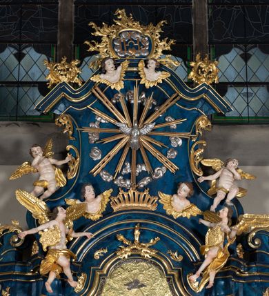 Zdjęcie nr 11: Nastawa architektoniczna, jednoosiowa, jednokondygnacyjna ze zwieńczeniem, ustawiona na wysokim cokole. Ołtarz drewniany, prostopadłościenny, o falistych bokach, mensa drewniana z marmurowym portatylem w drewnianej obudowie. Antepedium ujęte szeroką ramą dekorowaną płaskorzeźbionym motywem wieńca przepasanego wstęgą, w polu medalion z monogramem Marii ujęty wychodzącymi spod jego spodu wiązankami utworzonymi z suchego, wijącego się akantu z karbowaną wstęgą. Nastawa ujęta dwiema parami pilastrów, wewnętrzną z wolutowymi wspornikami w połowie wysokości trzonów oraz zewnętrzną parą o trzonach w formie spływów wolutowych przechodzących w silnie wysunięte do przodu partie cokołu, na których znajdują się postumenty dla figur aniołów. Podpory dźwigają niepełne belkowanie wyłamane na ich osi, nad polem środkowym wyłącznie gzyms przyjmujący kształt łuku półkolistego. Na belkowaniu fragmenty przerwanego, falistego przyczółka oraz para aniołów z kartuszami. W polu środkowym wnęka w formie stojącego prostokąta zamkniętego łukiem segmentowym nadwieszonym z uskokiem, w profilowanej ramie z mniejszym obrazem Matki Boskiej z Dzieciątkiem w kształcie stojącego prostokąta. Poniżej gablota na wota w formie leżącego prostokąta ujęta profilowaną ramą. Kondygnacja flankowana uszami utworzonymi z rocaille'u. Zwieńczenie w formie zbliżonej do kwadratu o wklęsłych bokach przechodzących w woluty, na których siedzą putta, zamknięte fragmentem falistego gzymsu wyłamanego po bokach, na nim rokokowy kartusz z monogramem IHS w polu, flankowany rocaille'em. W polu zwieńczenia rzeźba gołębicy Ducha Świętego w glorii promienistej i otoku z obłoków, w towarzystwie czterech uskrzydlonych główek anielskich. Wszystkie pilastry oraz łuki dekorowane elementami rocaille'u. Struktura w całości polichromowana na sposób imitujący marmoryzację w kolorze niebieskim, ornamentyka i profile złocone, detal srebrzony. 
Wewnątrz skrzyni ołtarzowej napisy „MALOWAŁ LUDWIK WÓJCIK Z KRAKOWA 2 / XI 1914”; „LUDWIK WÓJCIK”; „MALOWALI STOPY”; „23.02.1994 / KONSERWOWALI / KAZIMIERZ PATEJUK / EWA I JERZY SUCHWAŁKO / Z WARSZAWY / PROBOSZCZOWAŁ / KS. BOLESŁAW WAWAK”. 