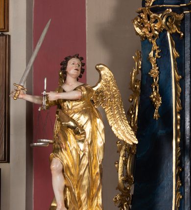 Zdjęcie nr 28: Nastawa architektoniczna, jednoosiowa, jednokondygnacyjna ze zwieńczeniem, ustawiona na wysokim cokole. Ołtarz drewniany, prostopadłościenny, o falistych bokach, mensa drewniana z marmurowym portatylem w drewnianej obudowie. Antepedium ujęte szeroką ramą dekorowaną płaskorzeźbionym motywem wieńca przepasanego wstęgą, w polu medalion z monogramem Marii ujęty wychodzącymi spod jego spodu wiązankami utworzonymi z suchego, wijącego się akantu z karbowaną wstęgą. Nastawa ujęta dwiema parami pilastrów, wewnętrzną z wolutowymi wspornikami w połowie wysokości trzonów oraz zewnętrzną parą o trzonach w formie spływów wolutowych przechodzących w silnie wysunięte do przodu partie cokołu, na których znajdują się postumenty dla figur aniołów. Podpory dźwigają niepełne belkowanie wyłamane na ich osi, nad polem środkowym wyłącznie gzyms przyjmujący kształt łuku półkolistego. Na belkowaniu fragmenty przerwanego, falistego przyczółka oraz para aniołów z kartuszami. W polu środkowym wnęka w formie stojącego prostokąta zamkniętego łukiem segmentowym nadwieszonym z uskokiem, w profilowanej ramie z mniejszym obrazem Matki Boskiej z Dzieciątkiem w kształcie stojącego prostokąta. Poniżej gablota na wota w formie leżącego prostokąta ujęta profilowaną ramą. Kondygnacja flankowana uszami utworzonymi z rocaille&#039;u. Zwieńczenie w formie zbliżonej do kwadratu o wklęsłych bokach przechodzących w woluty, na których siedzą putta, zamknięte fragmentem falistego gzymsu wyłamanego po bokach, na nim rokokowy kartusz z monogramem IHS w polu, flankowany rocaille&#039;em. W polu zwieńczenia rzeźba gołębicy Ducha Świętego w glorii promienistej i otoku z obłoków, w towarzystwie czterech uskrzydlonych główek anielskich. Wszystkie pilastry oraz łuki dekorowane elementami rocaille&#039;u. Struktura w całości polichromowana na sposób imitujący marmoryzację w kolorze niebieskim, ornamentyka i profile złocone, detal srebrzony. 
Wewnątrz skrzyni ołtarzowej napisy „MALOWAŁ LUDWIK WÓJCIK Z KRAKOWA 2 / XI 1914”; „LUDWIK WÓJCIK”; „MALOWALI STOPY”; „23.02.1994 / KONSERWOWALI / KAZIMIERZ PATEJUK / EWA I JERZY SUCHWAŁKO / Z WARSZAWY / PROBOSZCZOWAŁ / KS. BOLESŁAW WAWAK”. 