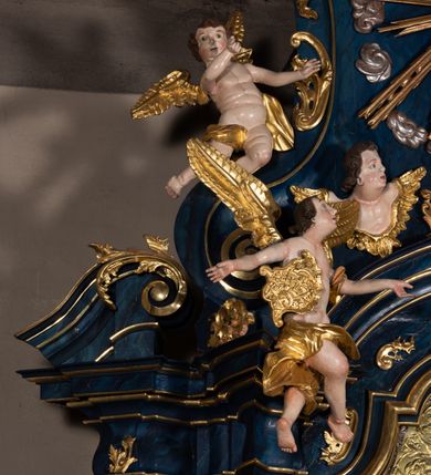 Zdjęcie nr 25: Nastawa architektoniczna, jednoosiowa, jednokondygnacyjna ze zwieńczeniem, ustawiona na wysokim cokole. Ołtarz drewniany, prostopadłościenny, o falistych bokach, mensa drewniana z marmurowym portatylem w drewnianej obudowie. Antepedium ujęte szeroką ramą dekorowaną płaskorzeźbionym motywem wieńca przepasanego wstęgą, w polu medalion z monogramem Marii ujęty wychodzącymi spod jego spodu wiązankami utworzonymi z suchego, wijącego się akantu z karbowaną wstęgą. Nastawa ujęta dwiema parami pilastrów, wewnętrzną z wolutowymi wspornikami w połowie wysokości trzonów oraz zewnętrzną parą o trzonach w formie spływów wolutowych przechodzących w silnie wysunięte do przodu partie cokołu, na których znajdują się postumenty dla figur aniołów. Podpory dźwigają niepełne belkowanie wyłamane na ich osi, nad polem środkowym wyłącznie gzyms przyjmujący kształt łuku półkolistego. Na belkowaniu fragmenty przerwanego, falistego przyczółka oraz para aniołów z kartuszami. W polu środkowym wnęka w formie stojącego prostokąta zamkniętego łukiem segmentowym nadwieszonym z uskokiem, w profilowanej ramie z mniejszym obrazem Matki Boskiej z Dzieciątkiem w kształcie stojącego prostokąta. Poniżej gablota na wota w formie leżącego prostokąta ujęta profilowaną ramą. Kondygnacja flankowana uszami utworzonymi z rocaille'u. Zwieńczenie w formie zbliżonej do kwadratu o wklęsłych bokach przechodzących w woluty, na których siedzą putta, zamknięte fragmentem falistego gzymsu wyłamanego po bokach, na nim rokokowy kartusz z monogramem IHS w polu, flankowany rocaille'em. W polu zwieńczenia rzeźba gołębicy Ducha Świętego w glorii promienistej i otoku z obłoków, w towarzystwie czterech uskrzydlonych główek anielskich. Wszystkie pilastry oraz łuki dekorowane elementami rocaille'u. Struktura w całości polichromowana na sposób imitujący marmoryzację w kolorze niebieskim, ornamentyka i profile złocone, detal srebrzony. 
Wewnątrz skrzyni ołtarzowej napisy „MALOWAŁ LUDWIK WÓJCIK Z KRAKOWA 2 / XI 1914”; „LUDWIK WÓJCIK”; „MALOWALI STOPY”; „23.02.1994 / KONSERWOWALI / KAZIMIERZ PATEJUK / EWA I JERZY SUCHWAŁKO / Z WARSZAWY / PROBOSZCZOWAŁ / KS. BOLESŁAW WAWAK”. 