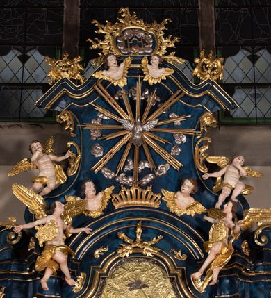 Zdjęcie nr 12: Nastawa architektoniczna, jednoosiowa, jednokondygnacyjna ze zwieńczeniem, ustawiona na wysokim cokole. Ołtarz drewniany, prostopadłościenny, o falistych bokach, mensa drewniana z marmurowym portatylem w drewnianej obudowie. Antepedium ujęte szeroką ramą dekorowaną płaskorzeźbionym motywem wieńca przepasanego wstęgą, w polu medalion z monogramem Marii ujęty wychodzącymi spod jego spodu wiązankami utworzonymi z suchego, wijącego się akantu z karbowaną wstęgą. Nastawa ujęta dwiema parami pilastrów, wewnętrzną z wolutowymi wspornikami w połowie wysokości trzonów oraz zewnętrzną parą o trzonach w formie spływów wolutowych przechodzących w silnie wysunięte do przodu partie cokołu, na których znajdują się postumenty dla figur aniołów. Podpory dźwigają niepełne belkowanie wyłamane na ich osi, nad polem środkowym wyłącznie gzyms przyjmujący kształt łuku półkolistego. Na belkowaniu fragmenty przerwanego, falistego przyczółka oraz para aniołów z kartuszami. W polu środkowym wnęka w formie stojącego prostokąta zamkniętego łukiem segmentowym nadwieszonym z uskokiem, w profilowanej ramie z mniejszym obrazem Matki Boskiej z Dzieciątkiem w kształcie stojącego prostokąta. Poniżej gablota na wota w formie leżącego prostokąta ujęta profilowaną ramą. Kondygnacja flankowana uszami utworzonymi z rocaille&#039;u. Zwieńczenie w formie zbliżonej do kwadratu o wklęsłych bokach przechodzących w woluty, na których siedzą putta, zamknięte fragmentem falistego gzymsu wyłamanego po bokach, na nim rokokowy kartusz z monogramem IHS w polu, flankowany rocaille&#039;em. W polu zwieńczenia rzeźba gołębicy Ducha Świętego w glorii promienistej i otoku z obłoków, w towarzystwie czterech uskrzydlonych główek anielskich. Wszystkie pilastry oraz łuki dekorowane elementami rocaille&#039;u. Struktura w całości polichromowana na sposób imitujący marmoryzację w kolorze niebieskim, ornamentyka i profile złocone, detal srebrzony. 
Wewnątrz skrzyni ołtarzowej napisy „MALOWAŁ LUDWIK WÓJCIK Z KRAKOWA 2 / XI 1914”; „LUDWIK WÓJCIK”; „MALOWALI STOPY”; „23.02.1994 / KONSERWOWALI / KAZIMIERZ PATEJUK / EWA I JERZY SUCHWAŁKO / Z WARSZAWY / PROBOSZCZOWAŁ / KS. BOLESŁAW WAWAK”. 