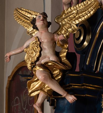 Zdjęcie nr 17: Nastawa architektoniczna, jednoosiowa, jednokondygnacyjna ze zwieńczeniem, ustawiona na wysokim cokole. Ołtarz drewniany, prostopadłościenny, o falistych bokach, mensa drewniana z marmurowym portatylem w drewnianej obudowie. Antepedium ujęte szeroką ramą dekorowaną płaskorzeźbionym motywem wieńca przepasanego wstęgą, w polu medalion z monogramem Marii ujęty wychodzącymi spod jego spodu wiązankami utworzonymi z suchego, wijącego się akantu z karbowaną wstęgą. Nastawa ujęta dwiema parami pilastrów, wewnętrzną z wolutowymi wspornikami w połowie wysokości trzonów oraz zewnętrzną parą o trzonach w formie spływów wolutowych przechodzących w silnie wysunięte do przodu partie cokołu, na których znajdują się postumenty dla figur aniołów. Podpory dźwigają niepełne belkowanie wyłamane na ich osi, nad polem środkowym wyłącznie gzyms przyjmujący kształt łuku półkolistego. Na belkowaniu fragmenty przerwanego, falistego przyczółka oraz para aniołów z kartuszami. W polu środkowym wnęka w formie stojącego prostokąta zamkniętego łukiem segmentowym nadwieszonym z uskokiem, w profilowanej ramie z mniejszym obrazem Matki Boskiej z Dzieciątkiem w kształcie stojącego prostokąta. Poniżej gablota na wota w formie leżącego prostokąta ujęta profilowaną ramą. Kondygnacja flankowana uszami utworzonymi z rocaille&#039;u. Zwieńczenie w formie zbliżonej do kwadratu o wklęsłych bokach przechodzących w woluty, na których siedzą putta, zamknięte fragmentem falistego gzymsu wyłamanego po bokach, na nim rokokowy kartusz z monogramem IHS w polu, flankowany rocaille&#039;em. W polu zwieńczenia rzeźba gołębicy Ducha Świętego w glorii promienistej i otoku z obłoków, w towarzystwie czterech uskrzydlonych główek anielskich. Wszystkie pilastry oraz łuki dekorowane elementami rocaille&#039;u. Struktura w całości polichromowana na sposób imitujący marmoryzację w kolorze niebieskim, ornamentyka i profile złocone, detal srebrzony. 
Wewnątrz skrzyni ołtarzowej napisy „MALOWAŁ LUDWIK WÓJCIK Z KRAKOWA 2 / XI 1914”; „LUDWIK WÓJCIK”; „MALOWALI STOPY”; „23.02.1994 / KONSERWOWALI / KAZIMIERZ PATEJUK / EWA I JERZY SUCHWAŁKO / Z WARSZAWY / PROBOSZCZOWAŁ / KS. BOLESŁAW WAWAK”. 